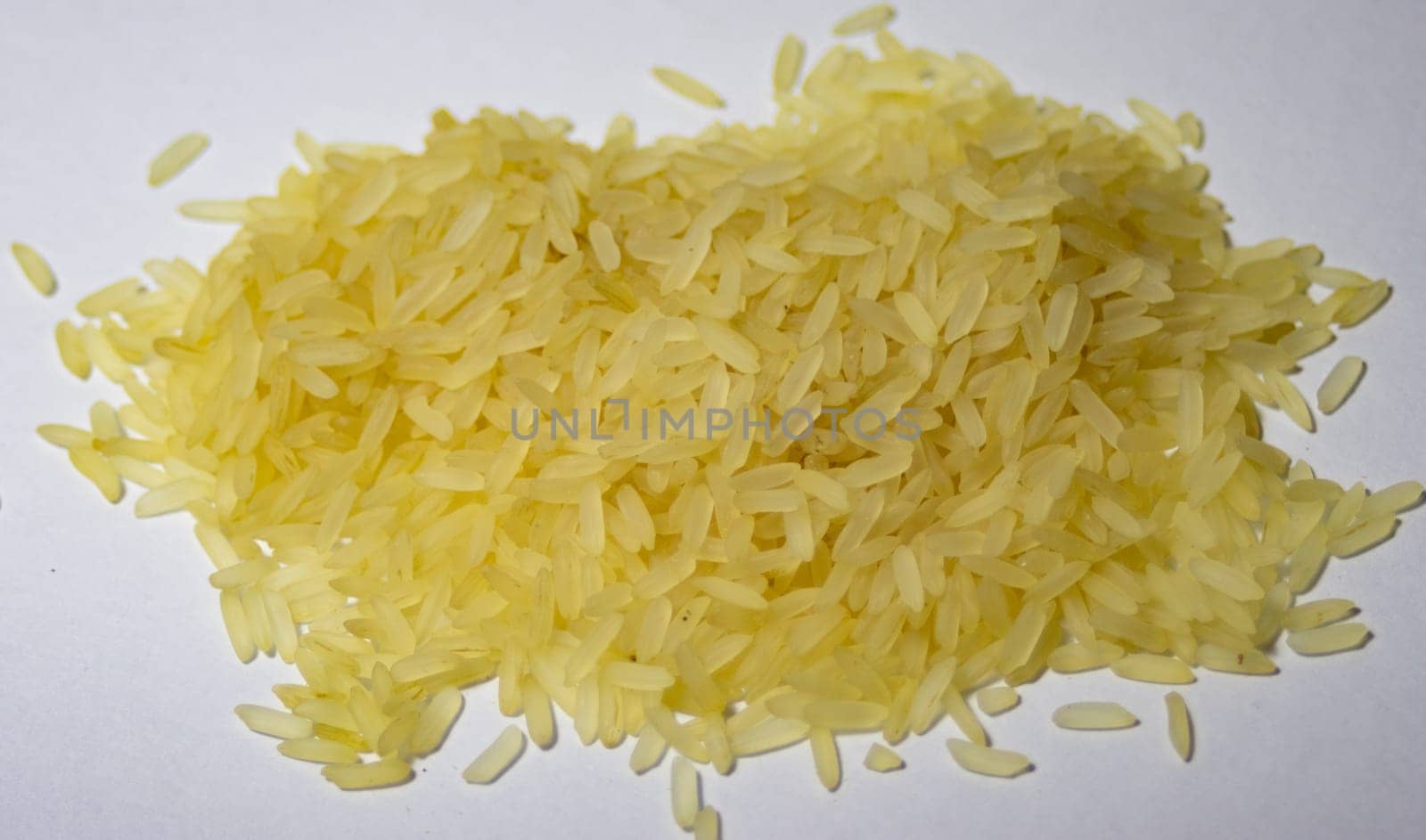 Very close-up photo of a pile of yellow parboiled rice on white background. by VeroDibe