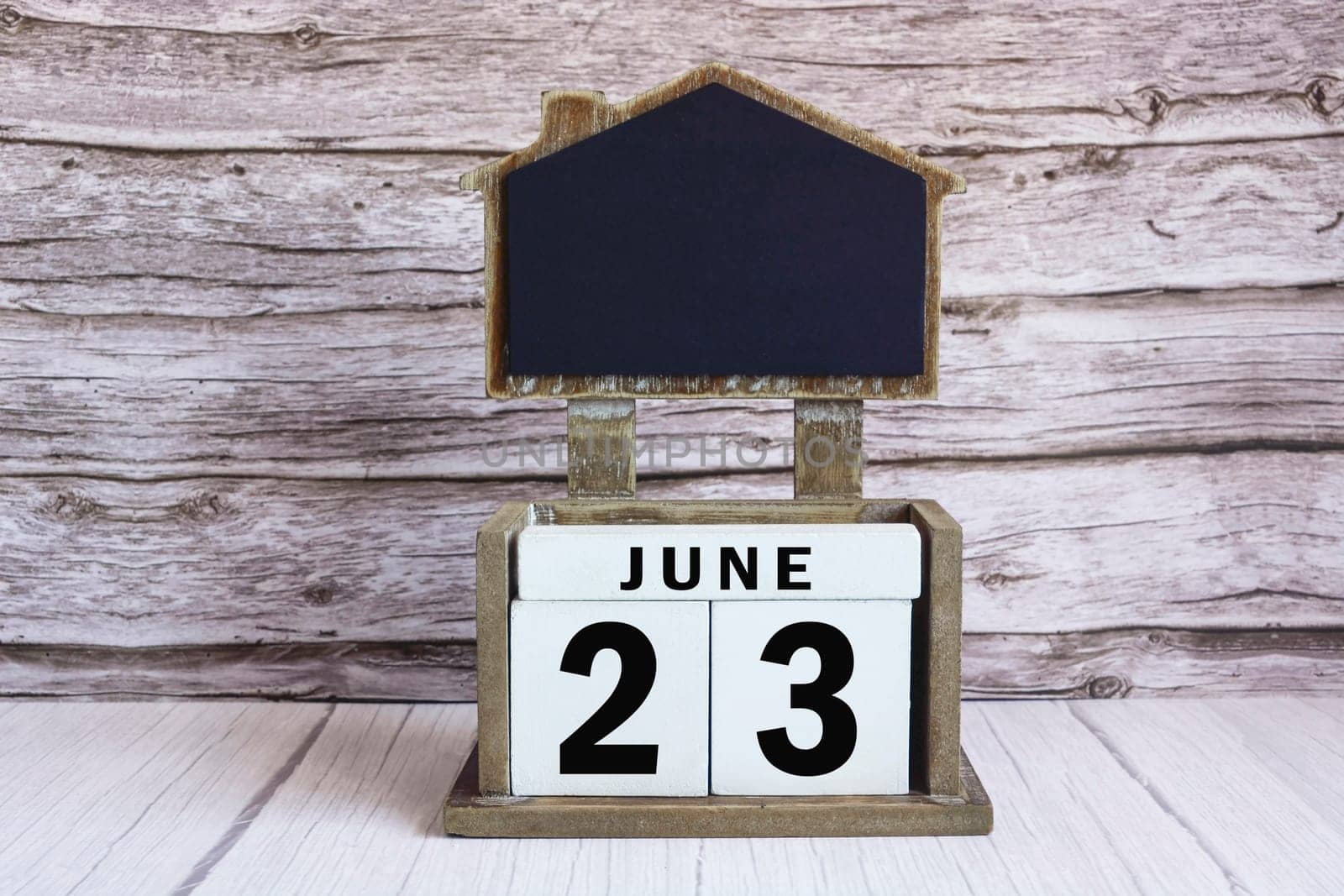 Chalkboard with June 23 calendar date on white cube block on wooden table.
