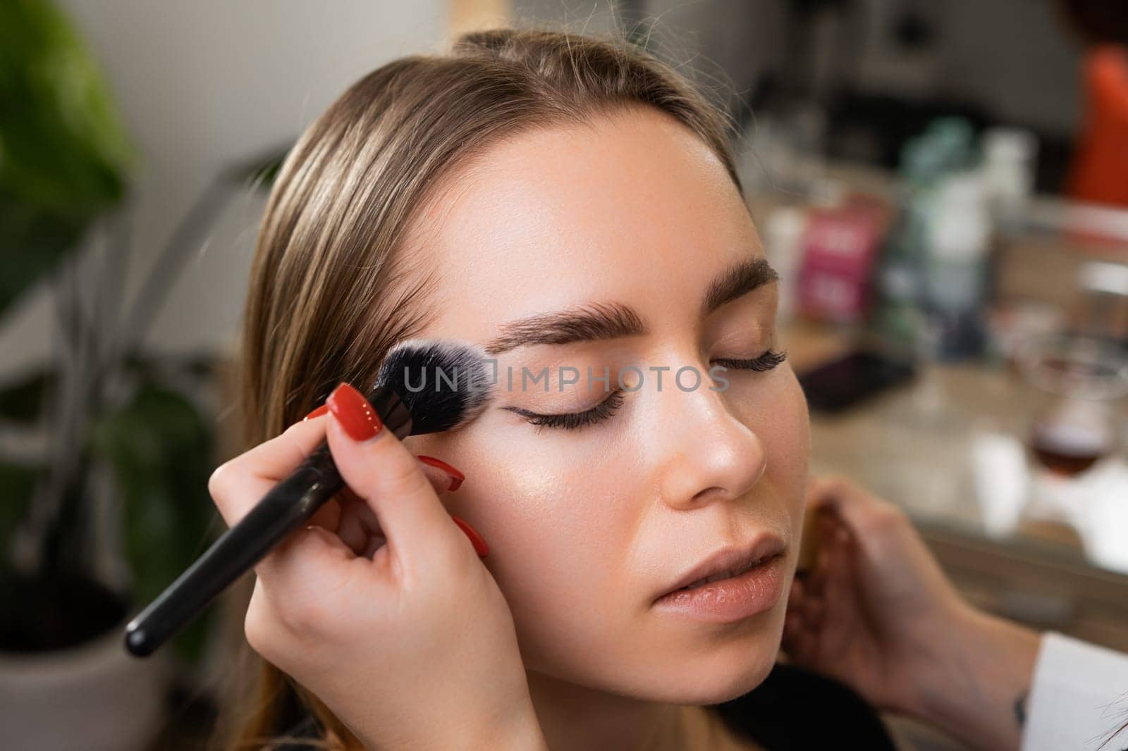 Woman makeup artist strategically layers facial powder on cheek. Professional provides young client durable base withstanding rigors of day
