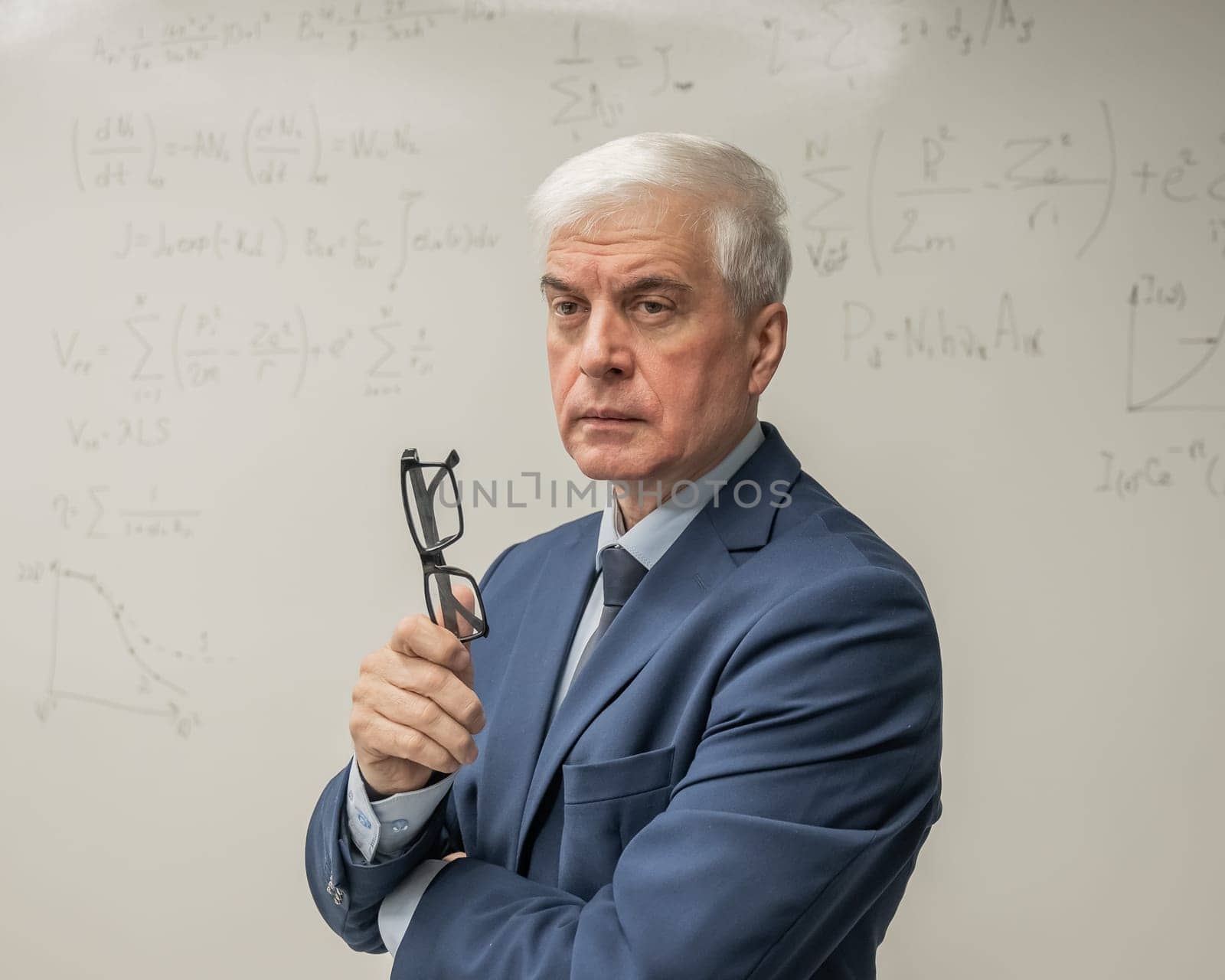 Mature man stands at a white board with written formulas. by mrwed54