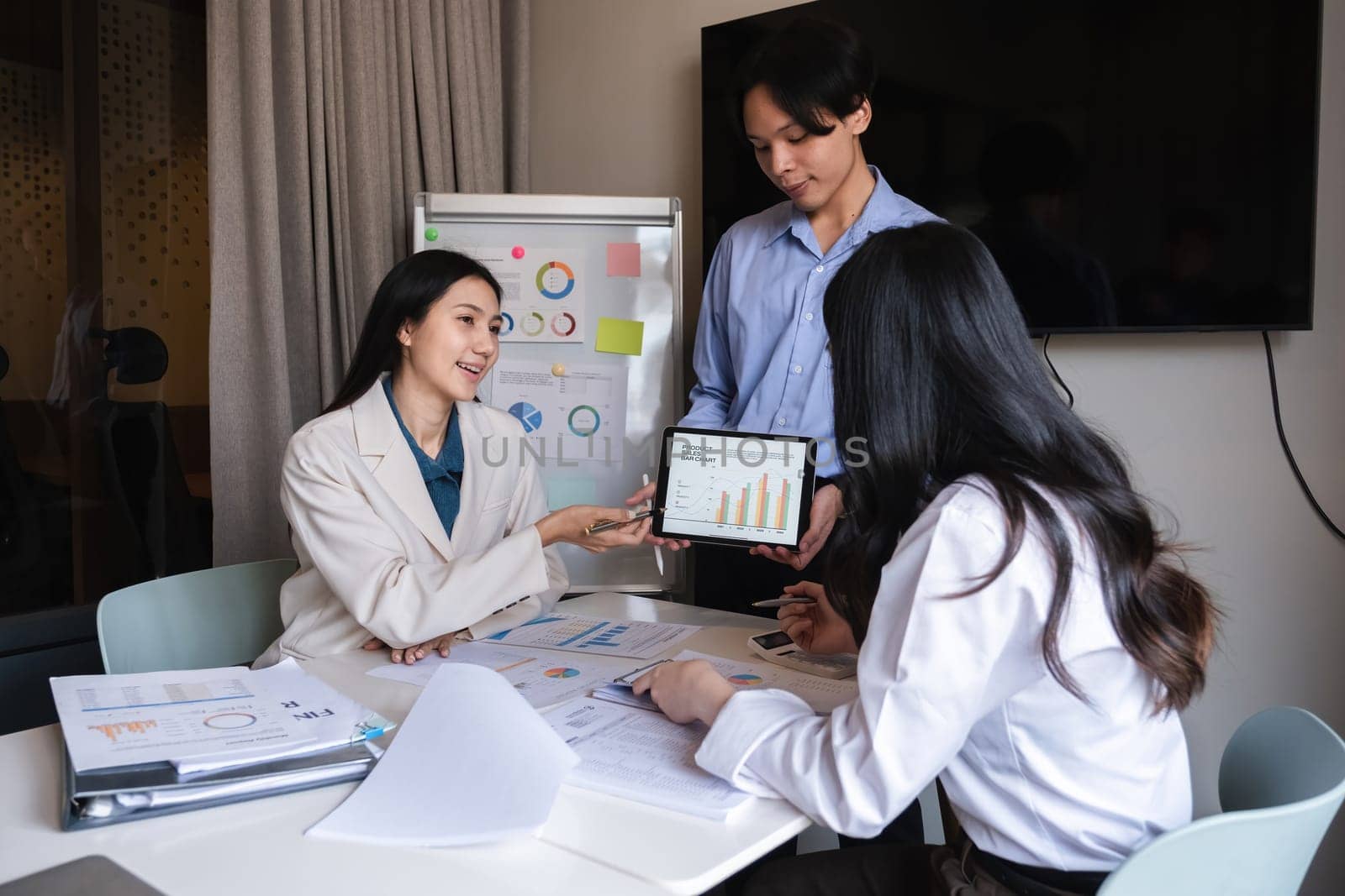 Young Asian business team discussing data analysis in modern office.