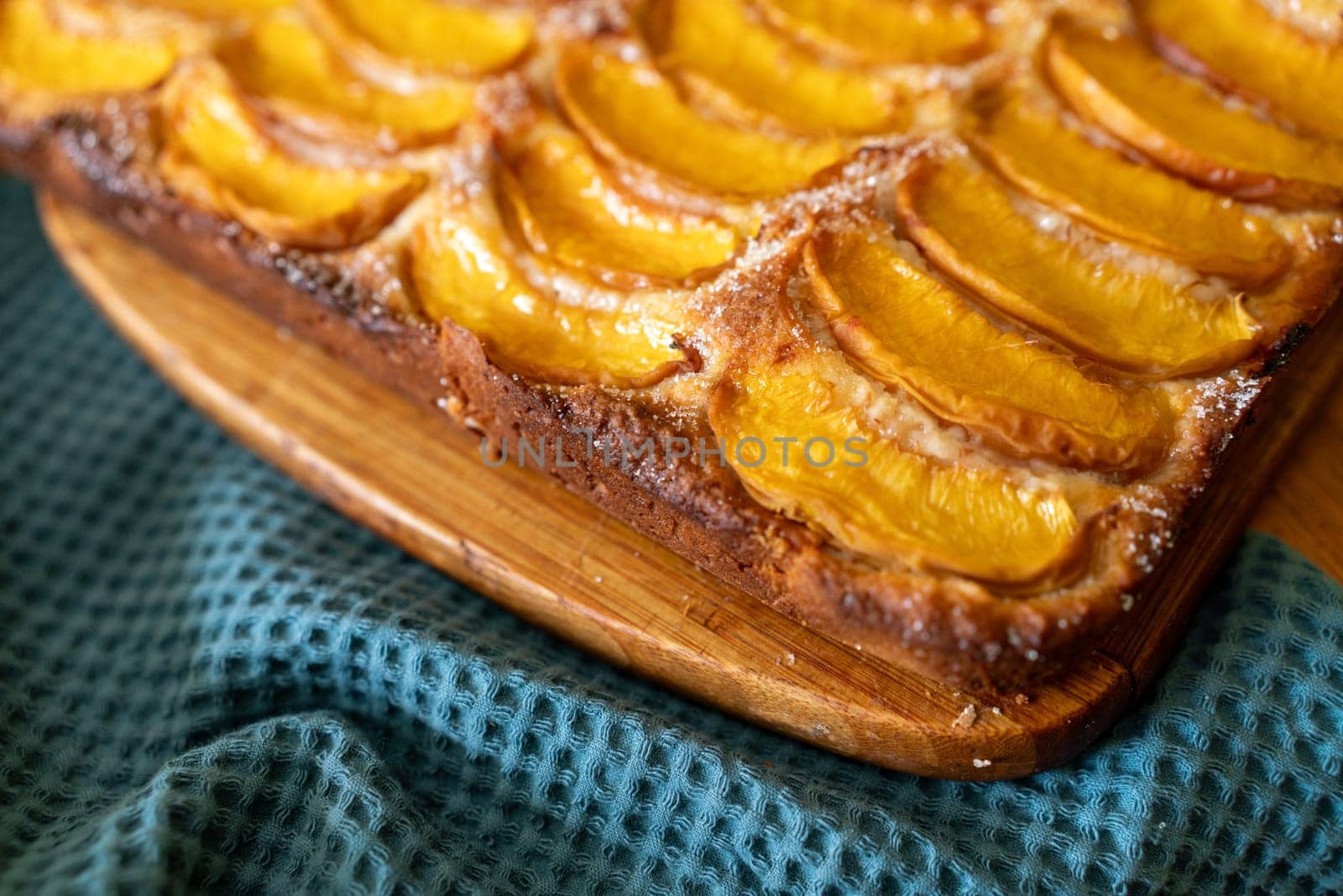 A dessert made of sliced peaches is on a wooden cutting board. The dessert is covered in sugar and looks delicious