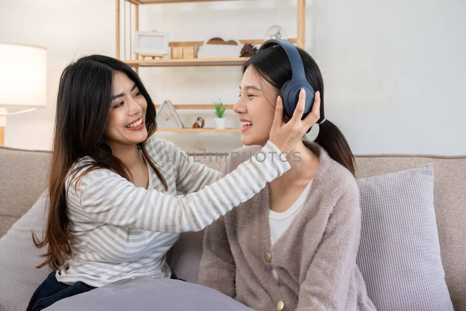 Two young women enjoying music together with headphones at home. Concept of friendship and shared enjoyment by wichayada