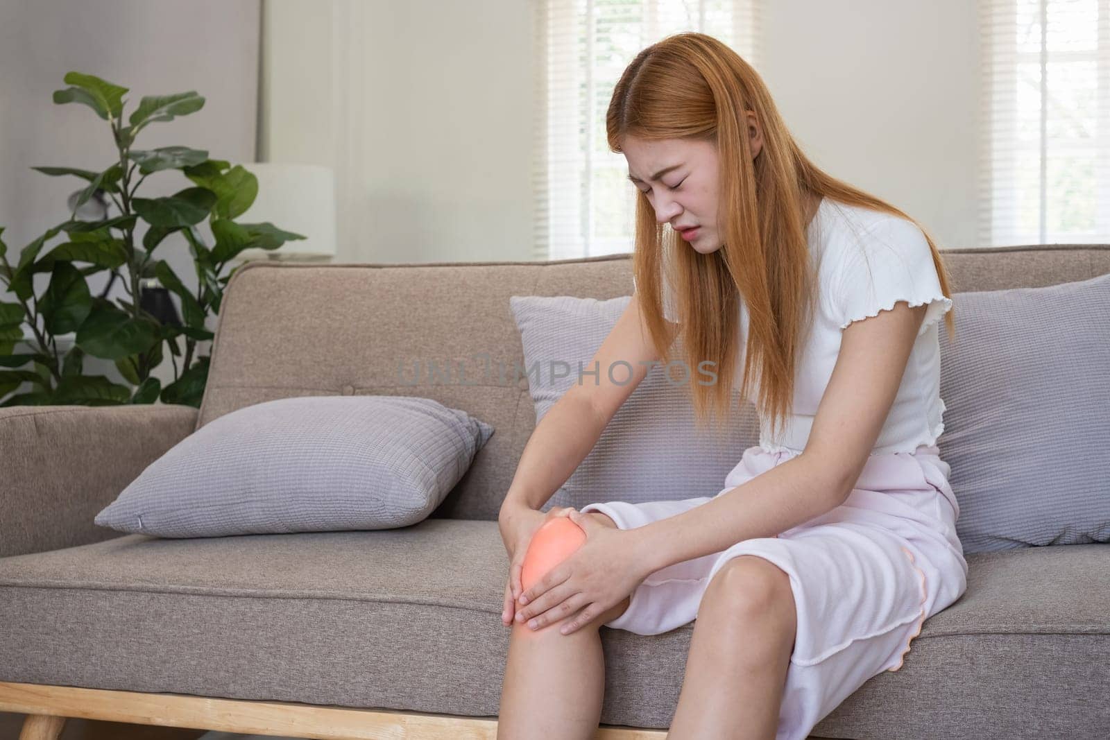 Asian woman experiencing knee pain at home. Concept of joint discomfort, pain relief, and health issues.