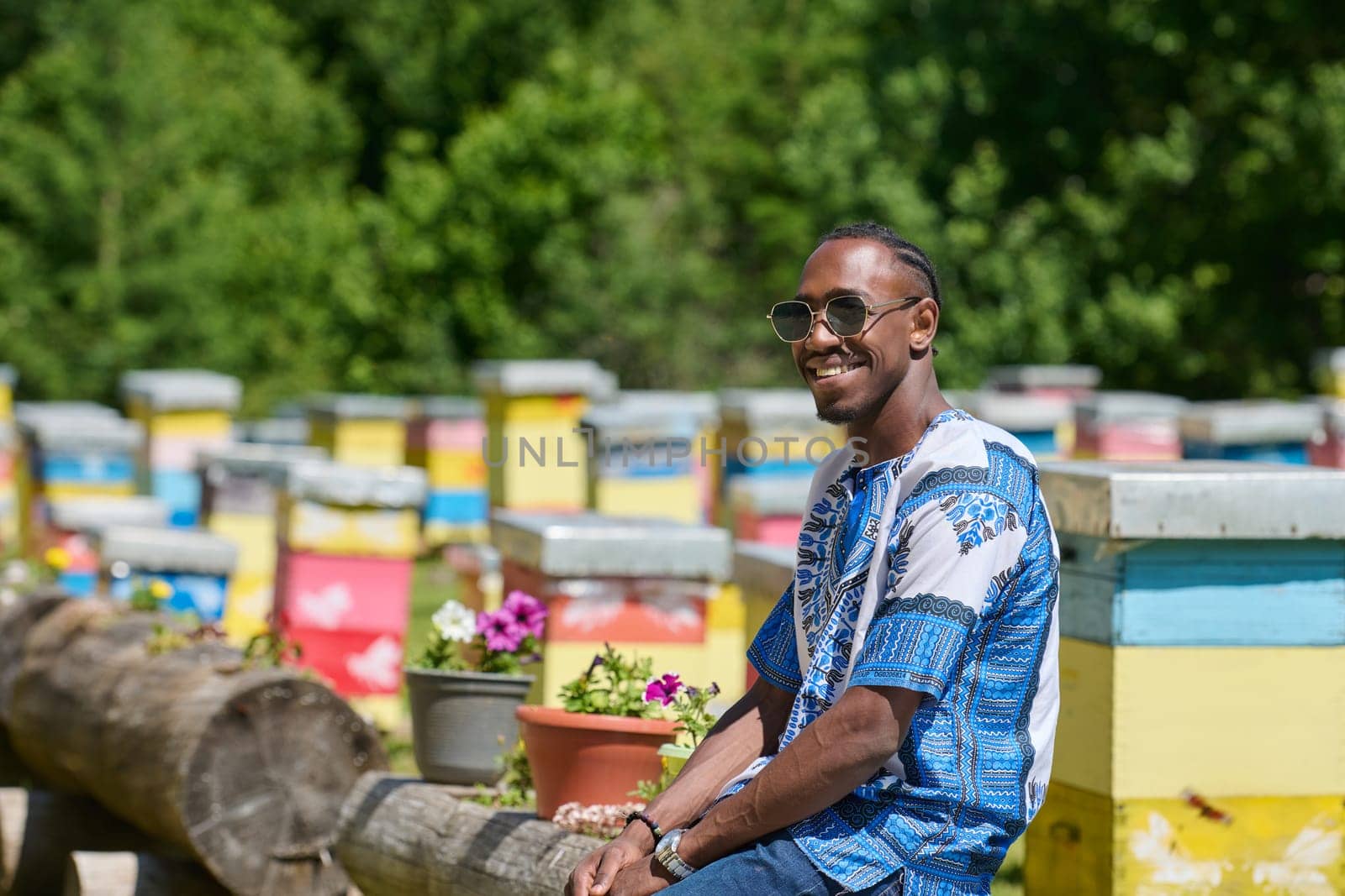 African American teenager clad in traditional Sudanese attire explores small beekeeping businesses amidst the beauty of nature