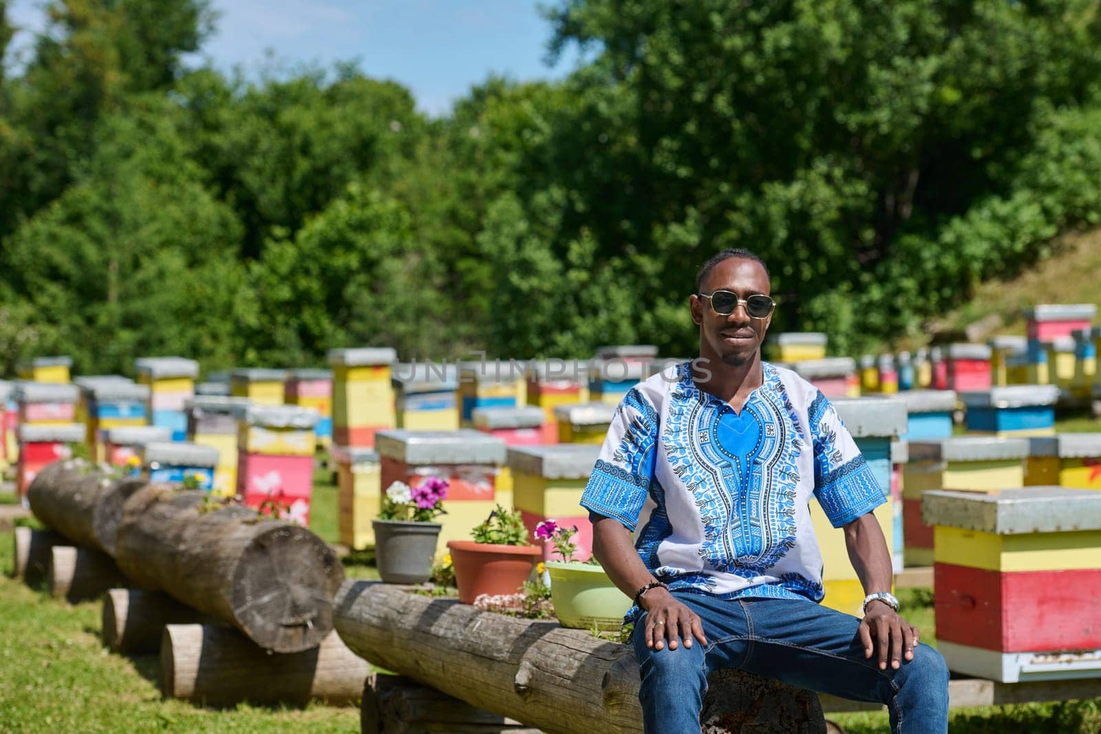 African American teenager clad in traditional Sudanese attire explores small beekeeping businesses amidst the beauty of nature