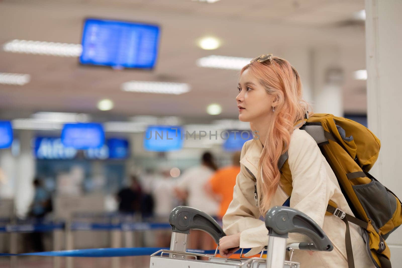 Young traveler with luggage cart and backpack at airport terminal. Concept of travel, exploration, and excitement by wichayada