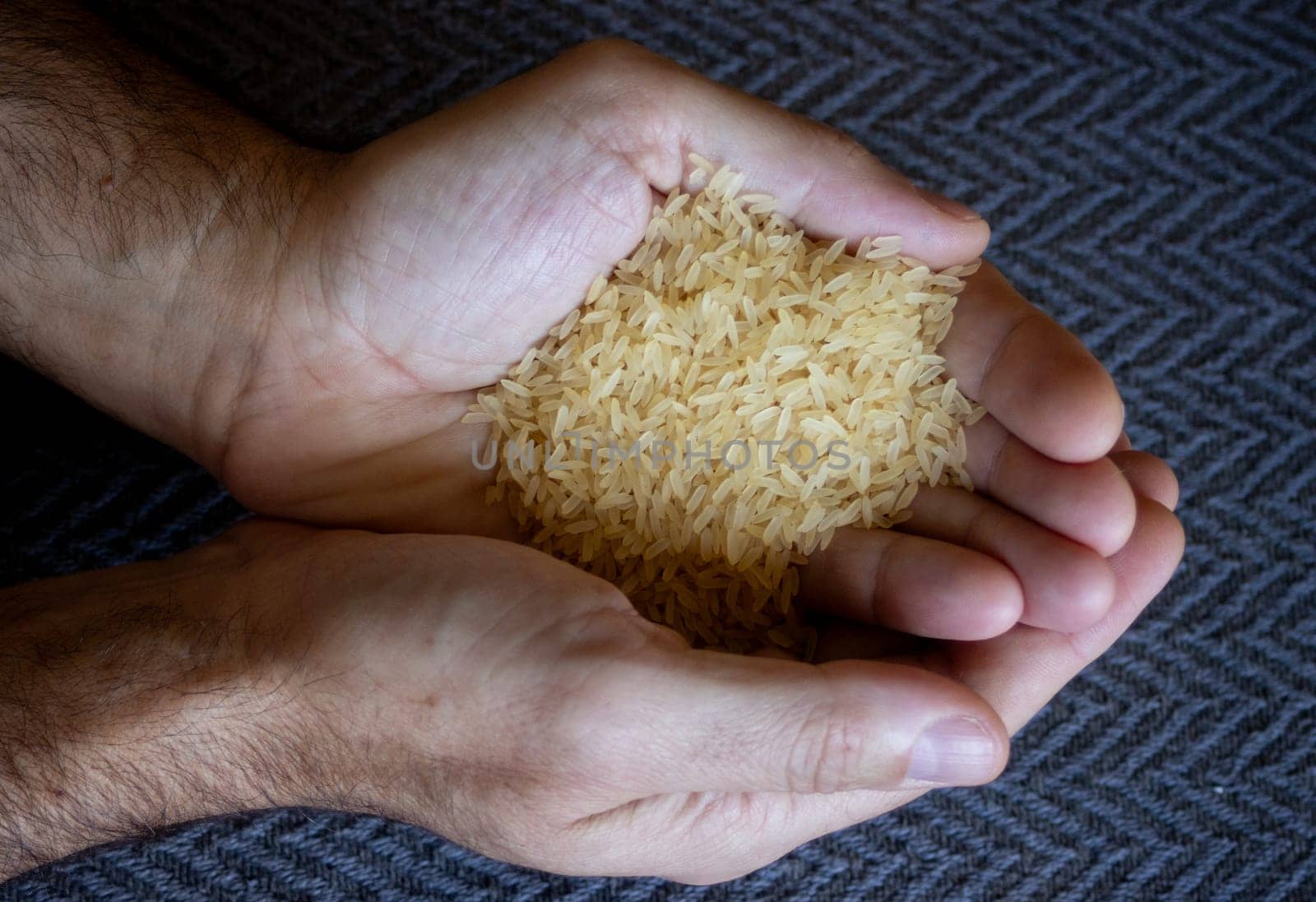 Horizontal photo of hands holding prboiled yellow rice grains.Dark background by VeroDibe