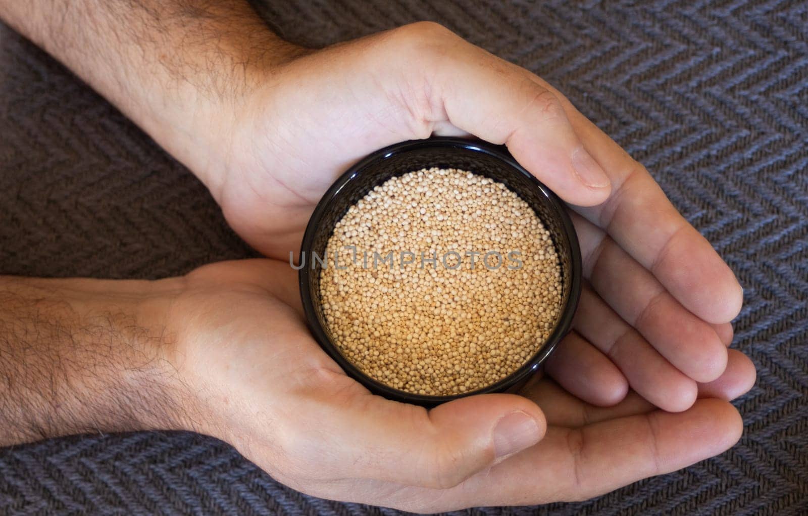 Hands holding a bowl of quinoa seeds.Dark background.Isolated by VeroDibe