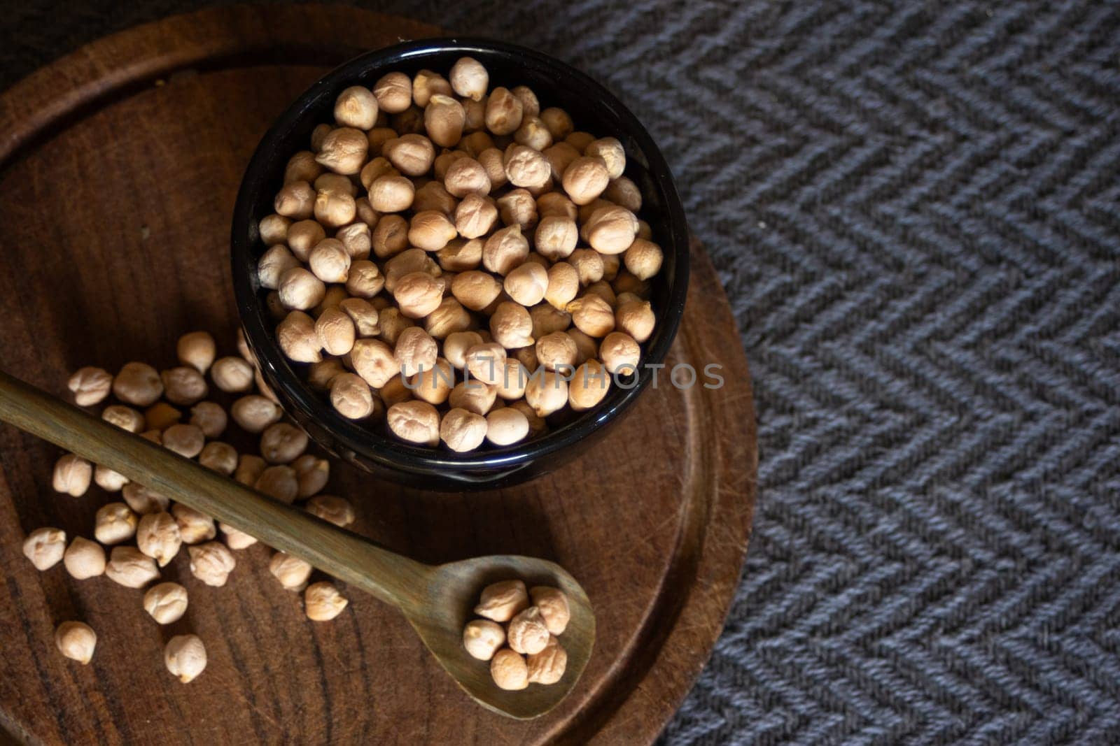 Chickpeas in black bowl and over wooden spoon Dark background. Copy space by VeroDibe