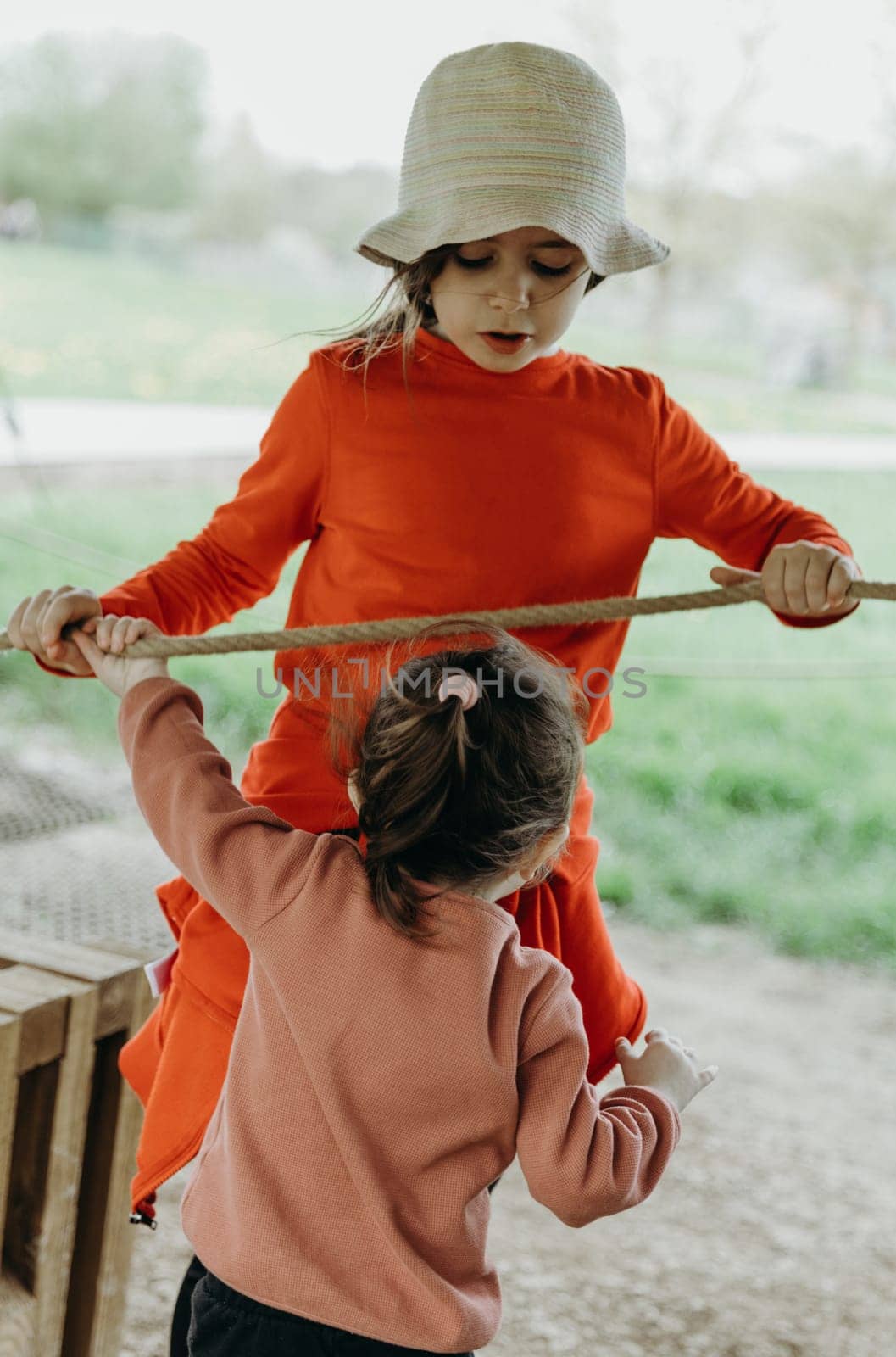 Portrait of two little beautiful Caucasian girls sisters actively and cheerfully playing tug of war on a spring day in a park in Belgium, close-up side view.