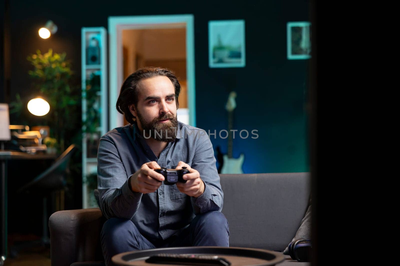 Joyous man playing videogame in home theatre, holding controller. Smiling gamer participating in PvP online multiplayer game using console system and high quality gamepad