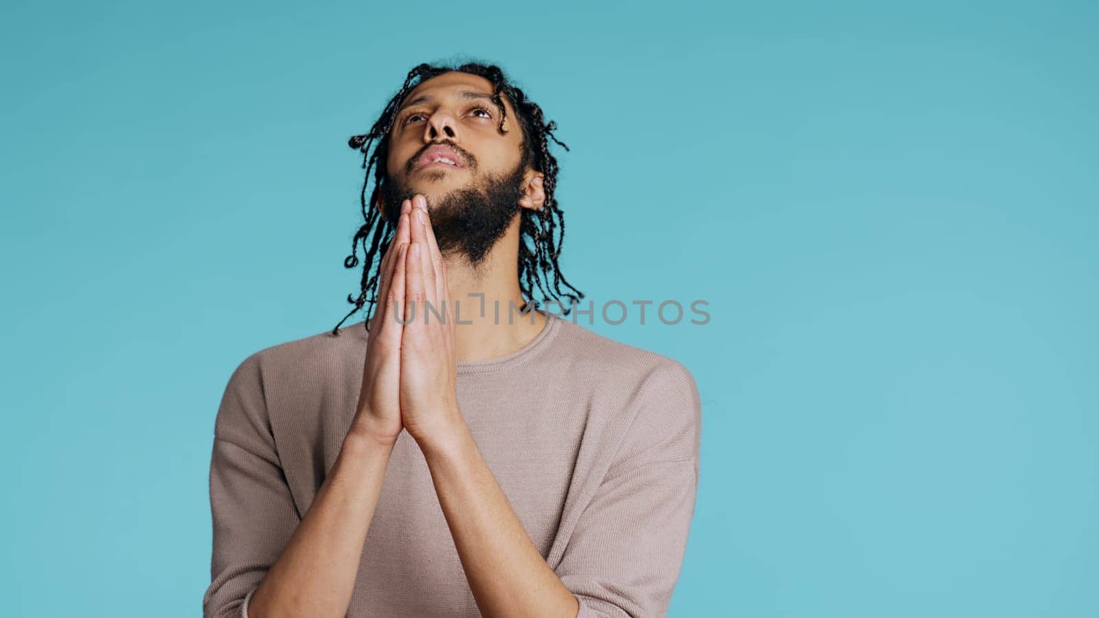 Pious Middle Eastern man praying to his god, asking for forgiveness, feeling desperate. Spiritual BIPOC man doing worship hand gesturing, confessing, begging for pardon, studio background, camera B