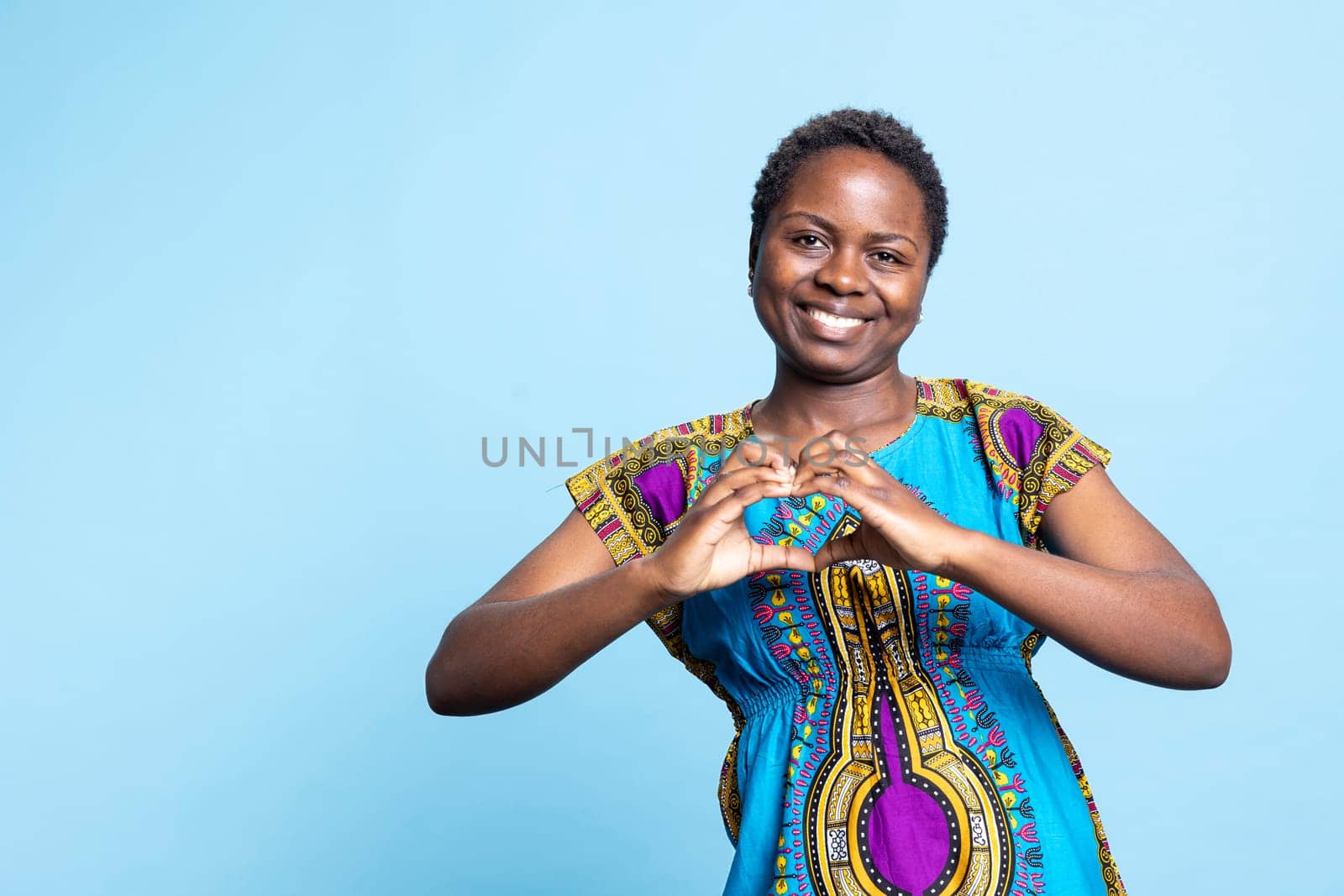 Young person creating heart shape gesture in the studio, expressing her sincere emotions with a romantic symbol. African american woman feeling optimistic, true love and feelings.