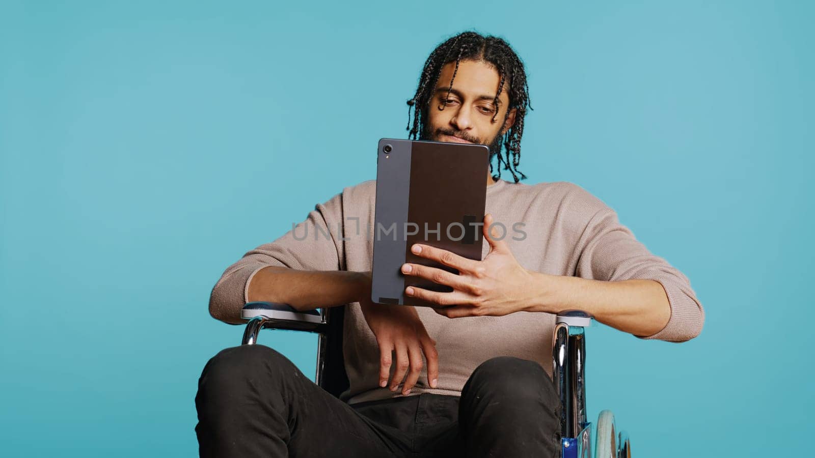 Man in wheelchair chatting with friend over internet videocall using tablet by DCStudio