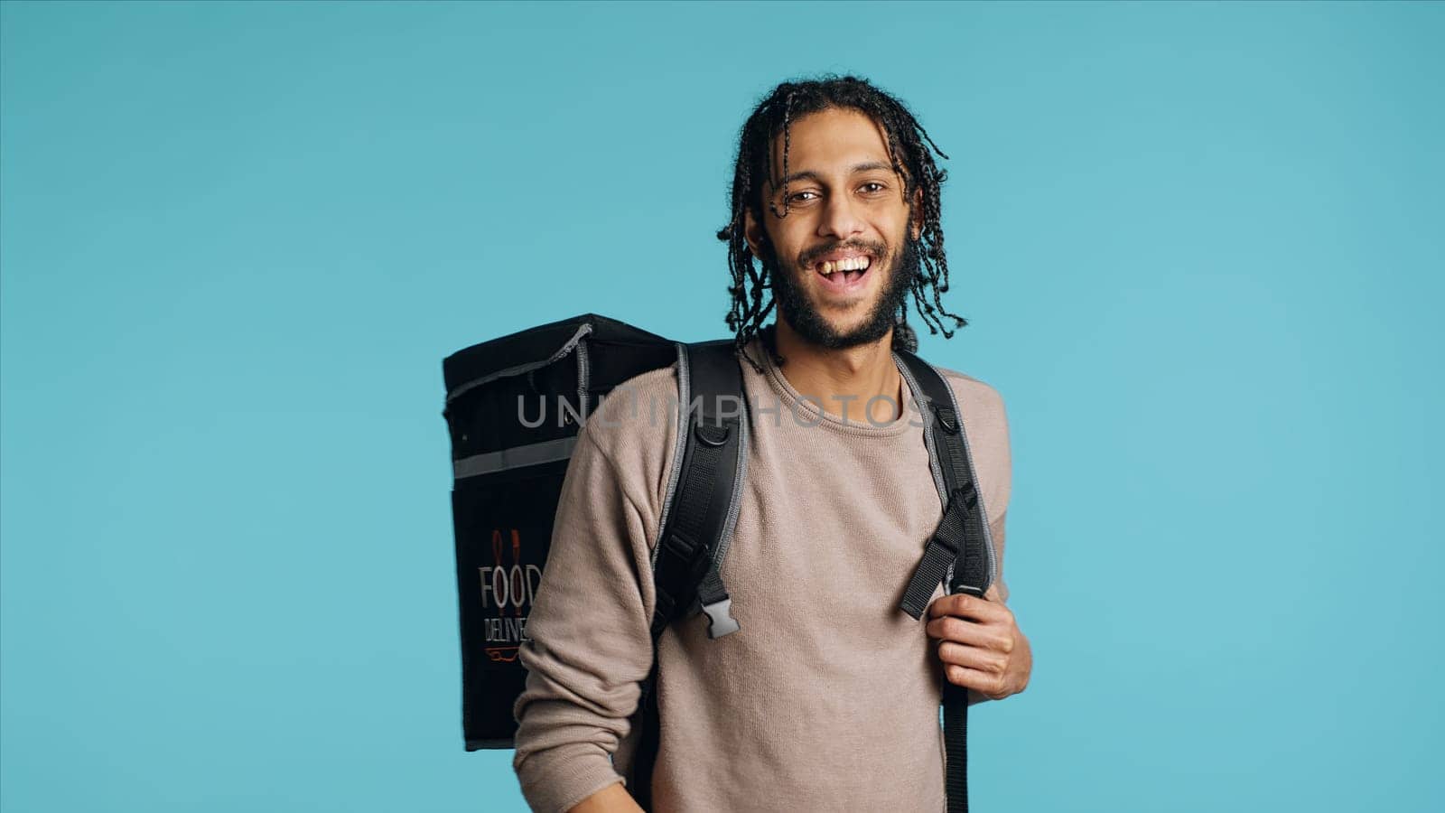 Portrait of cheerful courier waving hand, greeting client, bringing pizza box. Happy delivery part time employee using thermal backpack to bring food order to customer, studio background, camera A