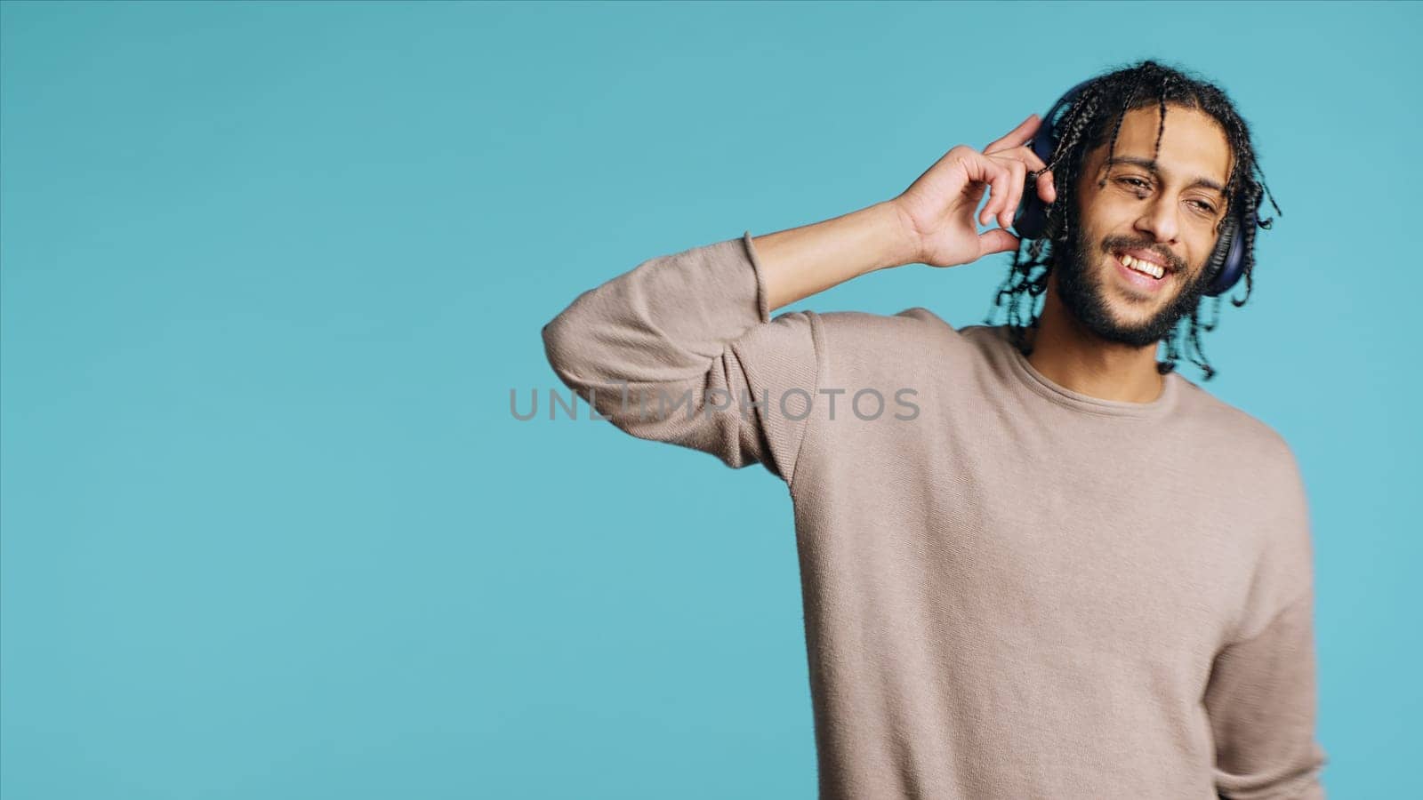 Joyous Middle Eastern man listening music, having fun, dancing on rhythm, enjoying leisure time. Upbeat BIPOC person wearing headphones, doing funky movements, studio background, camera A