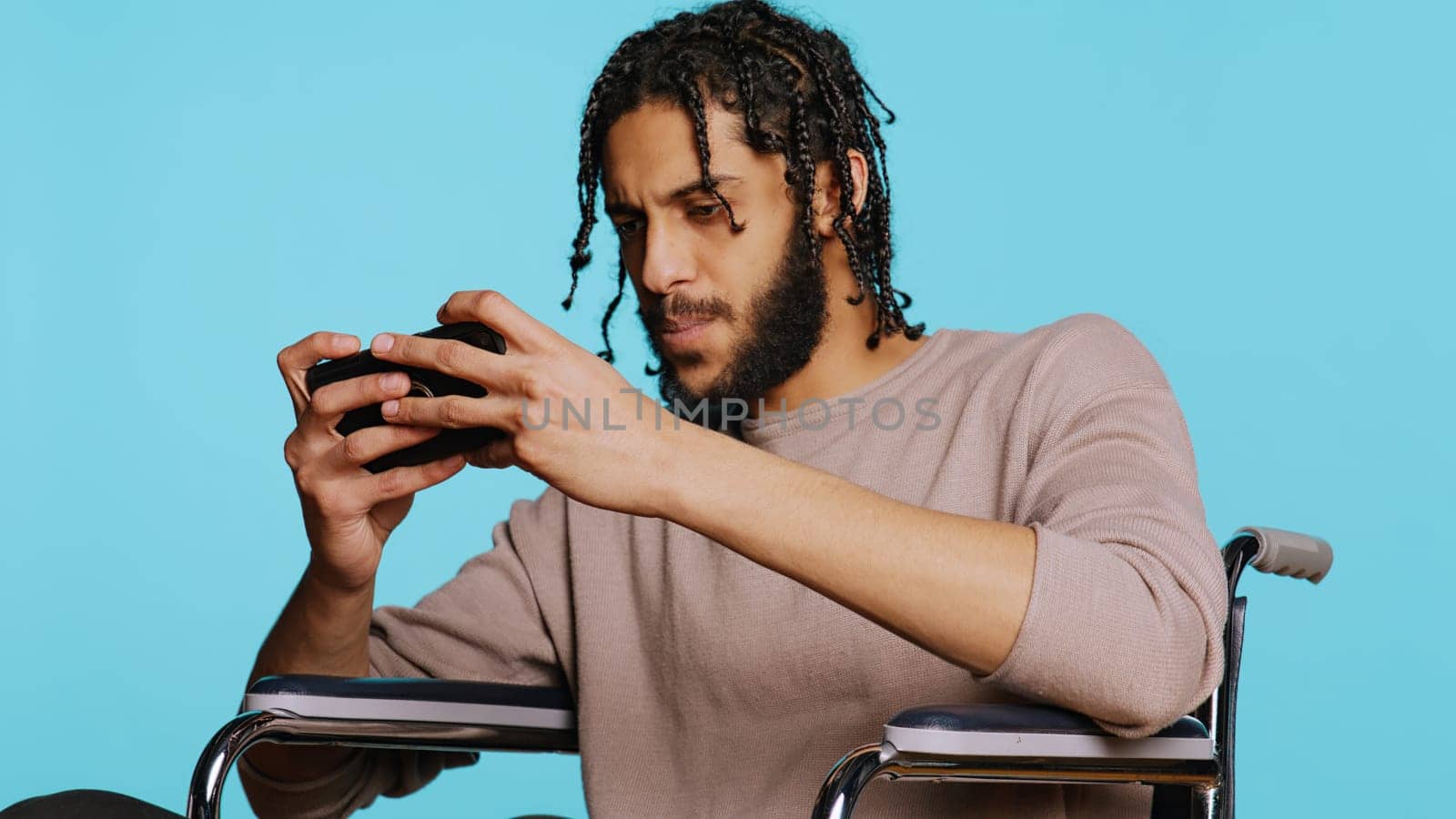 Happy man with disability in wheelchair playing videogames on cellphone, celebrating victory. Cheerful gamer enjoying game on phone, excited about win, studio background, camera B