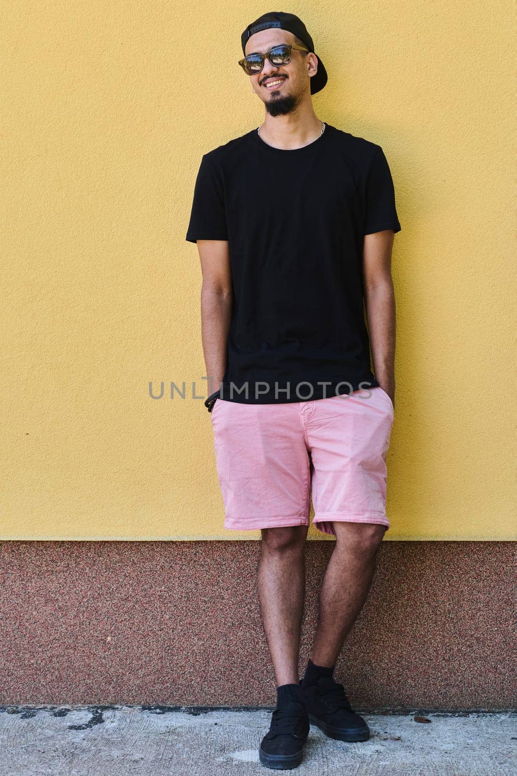 A depiction of urban coolness: a Middle Eastern teenager leaning against a yellow wall, exuding confidence in casual attire.