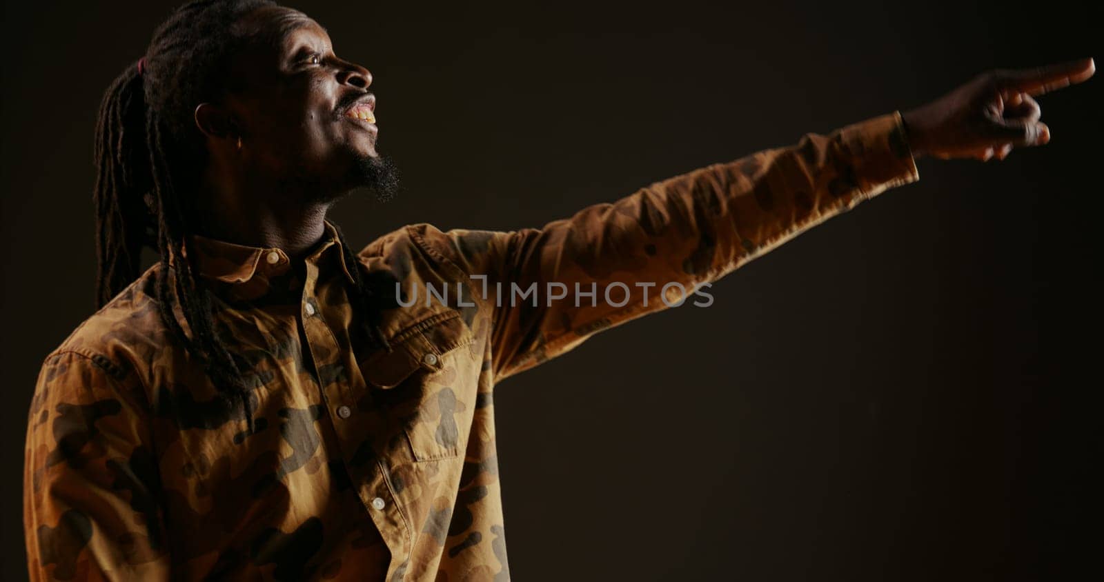 African american guy cheers for someone in studio, supporting and encouraging person over black background. Adult feeling confident and optimistic, celebrating victory and triumph. Handheld shot.