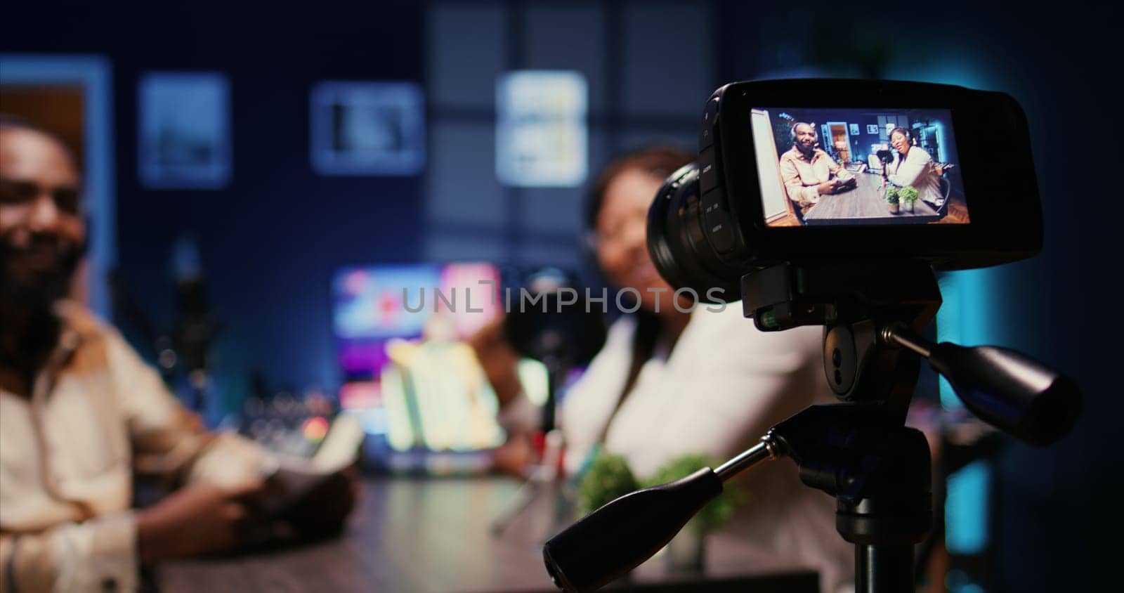 Focus on camera recording man on podcast in blurry background talking with guest during marathon stream for humanitarian cause. Close up of professional gear filming host during internet show