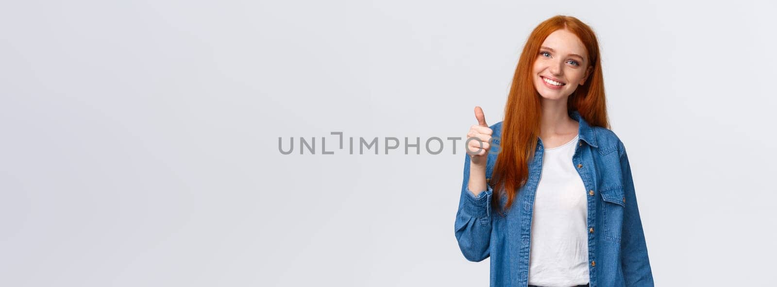 Well done, proud you. Attractive cheerful redhead caucasian girl blogger, review product, encourage friend keep up, showing thumb-up and smiling in approval, agree or like gesture, white background by Benzoix