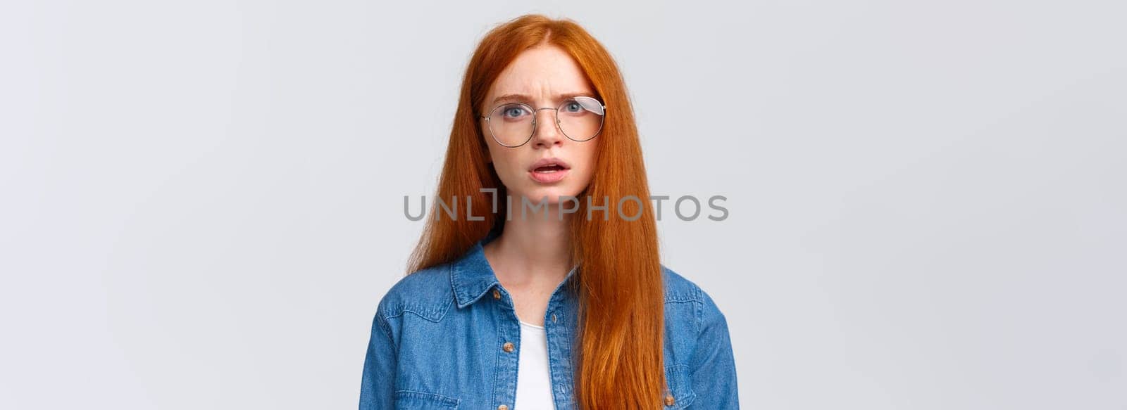 Confused and displeased, unsure redhead girl in glasses having conversation, talking look frustrated and slightly unconvinced, have doubts standing white background frowning.