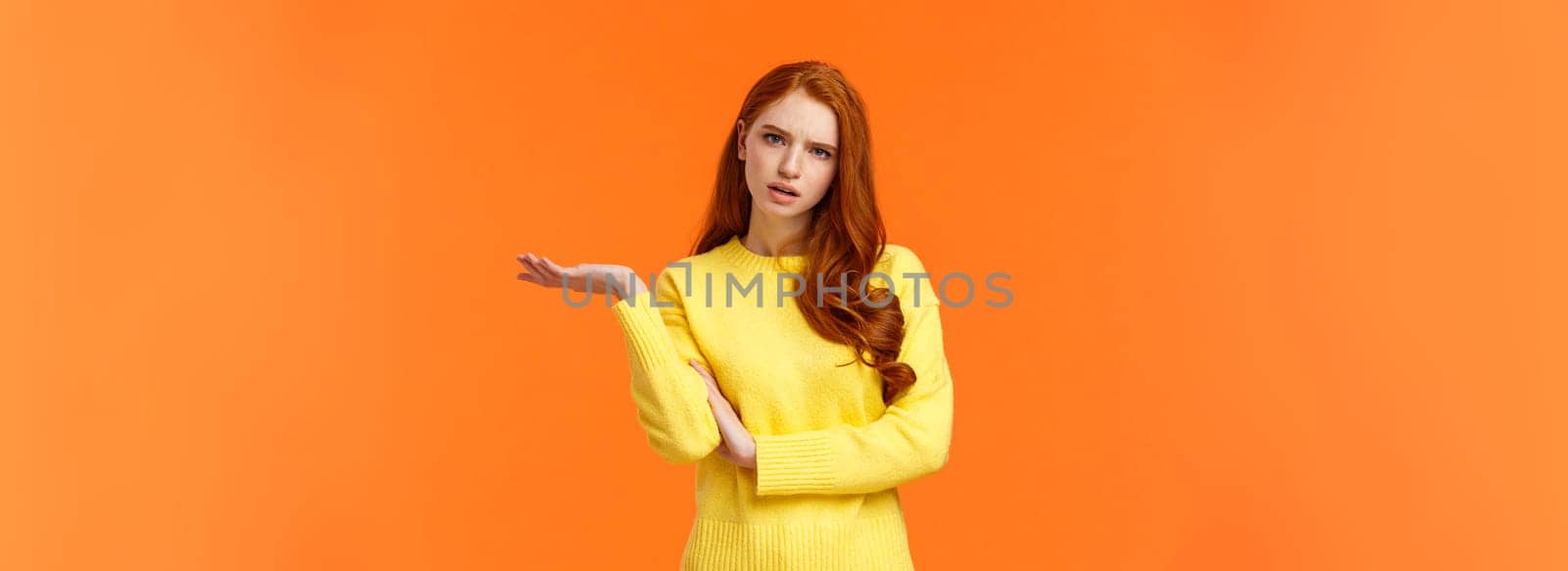 Skeptical and troubled, uncertain young redhead woman cant understand how resolve proble, shrugging raise hands sideways, frowning confused or unsure, standing frustrated orange background by Benzoix