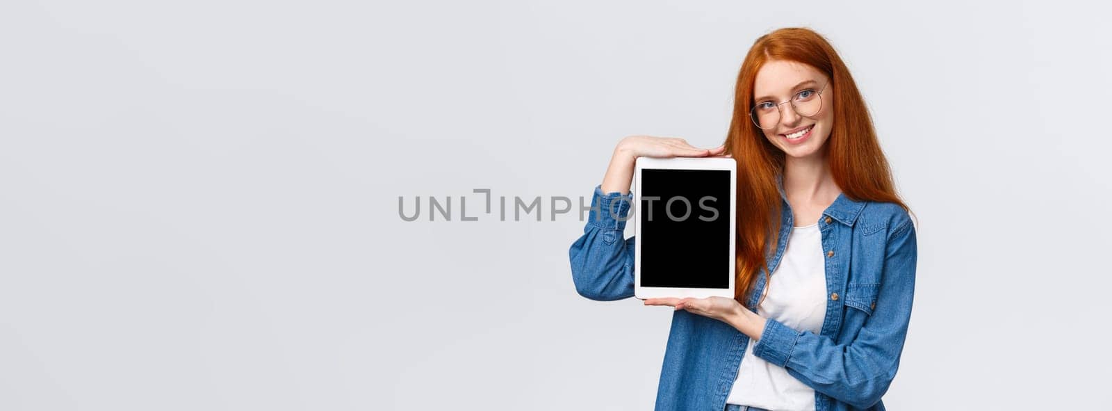 Waist-up attractive confident female with red hair, blue eyes in glasses, introduce application, presenting new app, holding digital tablet and showing gadget display, smiling recommend download by Benzoix