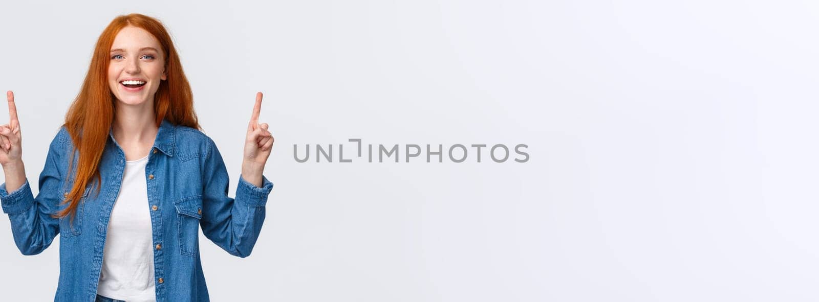 Cheerful outgoing alluring redhead woman, long red hairstyle, showing top promo, pointing fingers up and laughing, smiling amused, leave positive review, blogger visit awesome place, white background.