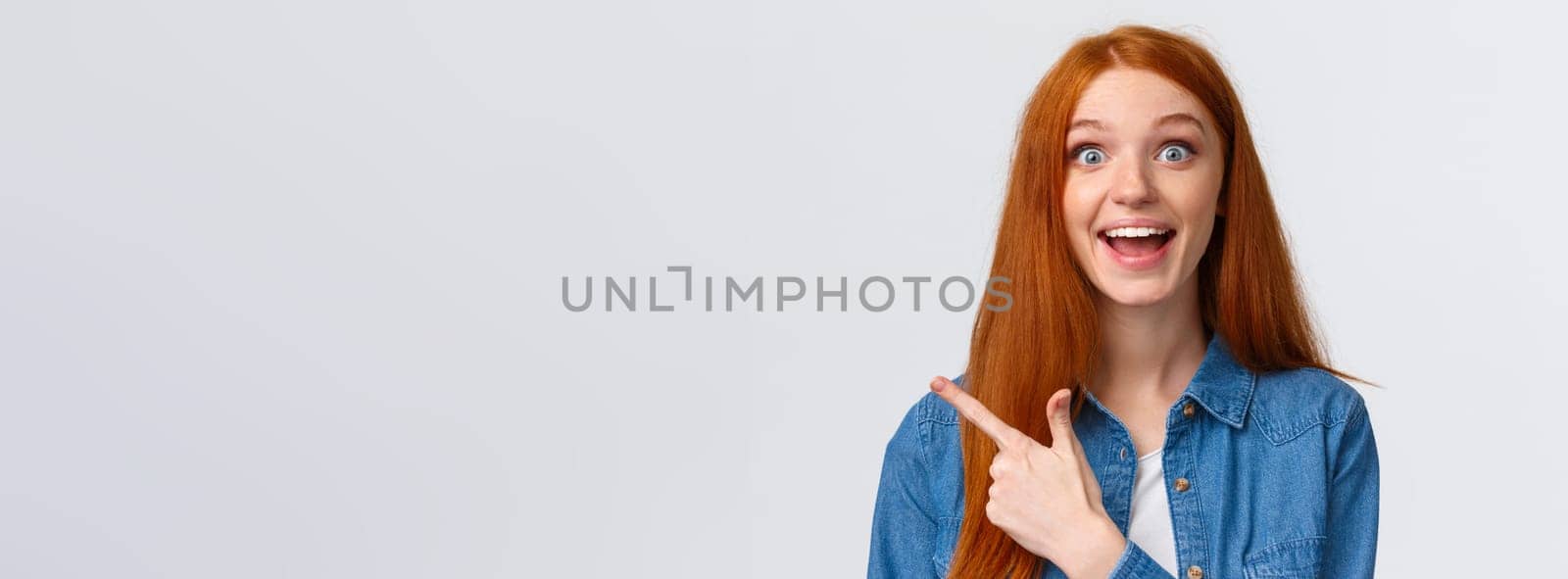 Close-up portrait excited happy ginger girl, foxy hair and blue eyes, smiling upbeat with amazement and joy, pointing finger left, attend amusing cool party, telling about it, white background by Benzoix