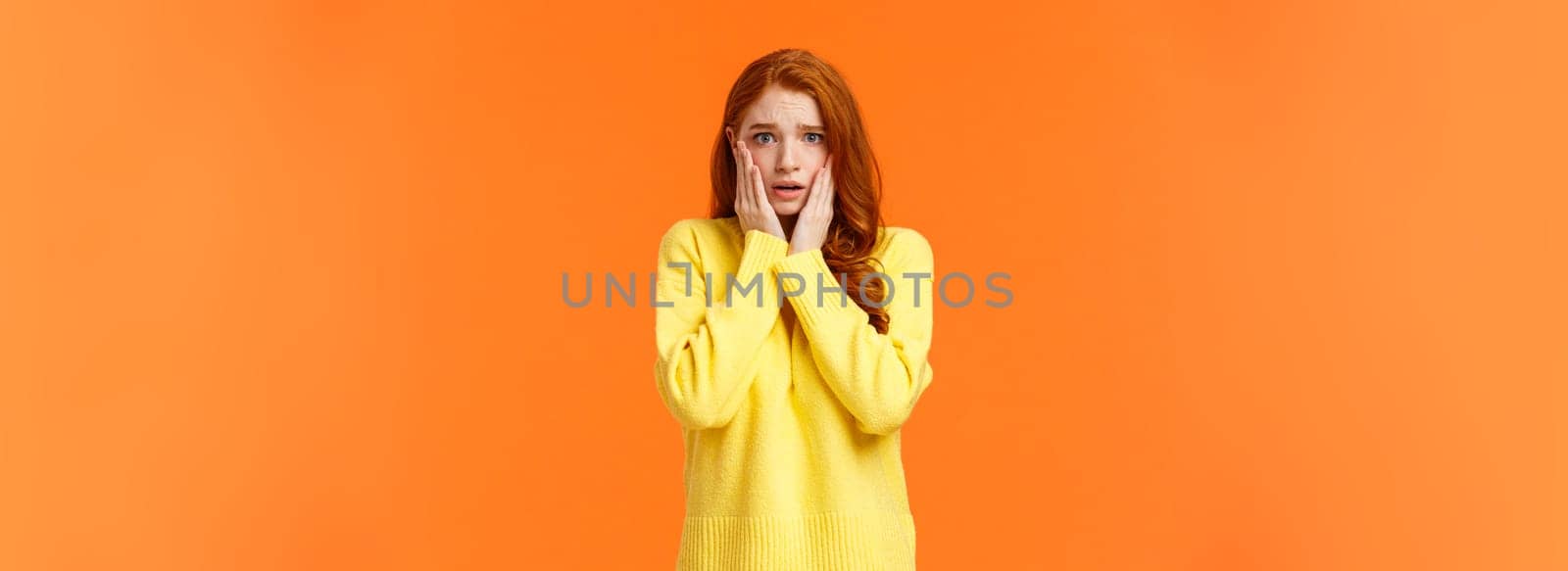 Concerned and anxious redhead girl forgot take chicken out freezer before mom came home, grab face, gasping scared and troubled, dont know what do, standing tensed and afraid, orange background by Benzoix