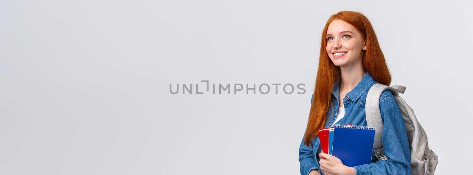 Youth, teenagers and education concept. Determined good-looking dreamy and upbeat smiling redhead female student with notebooks and backpack looking forward new theme in class by Benzoix