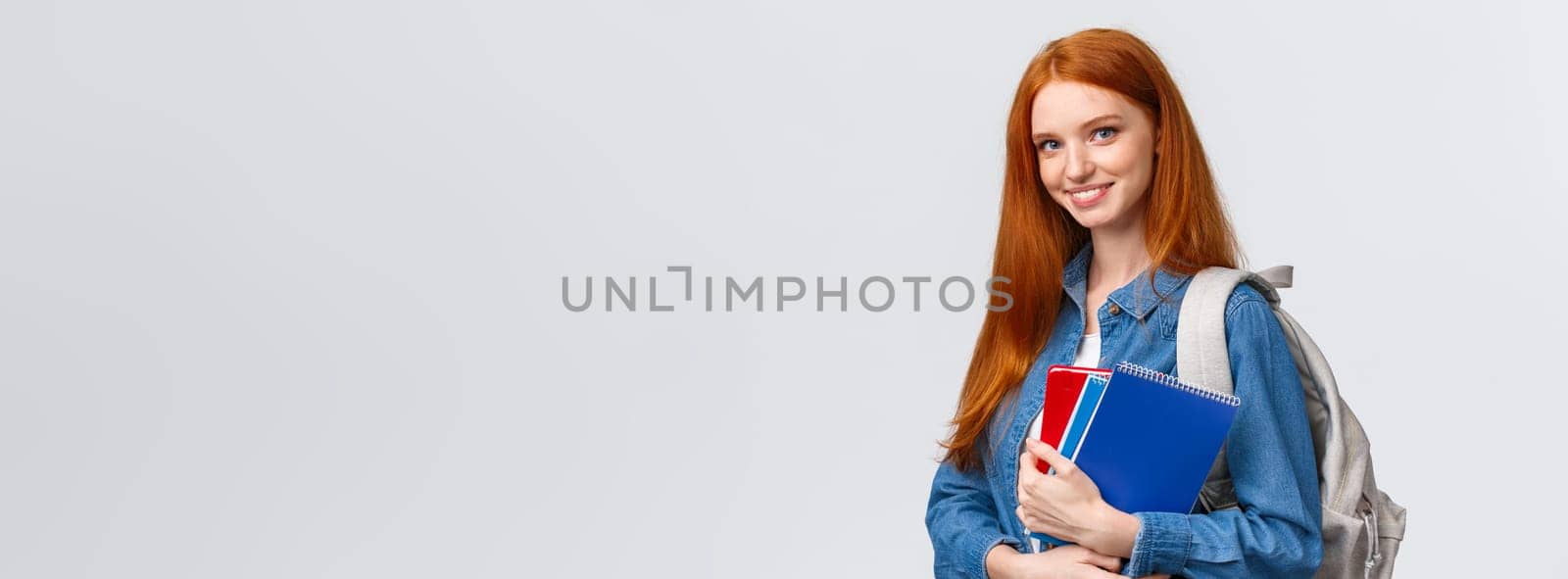 Time to school. Lovely cheerful modern redhead female with backpack holding notebooks heading college, smiling amused, heading back to class after break, standing white background.