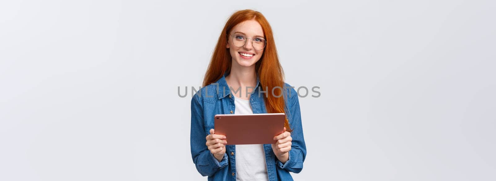 Education, people and teamwork concept. Cheerful pretty redhead millennial female coworker introducing project to team, holding digital tablet, wearing glasses, smiling at camera.