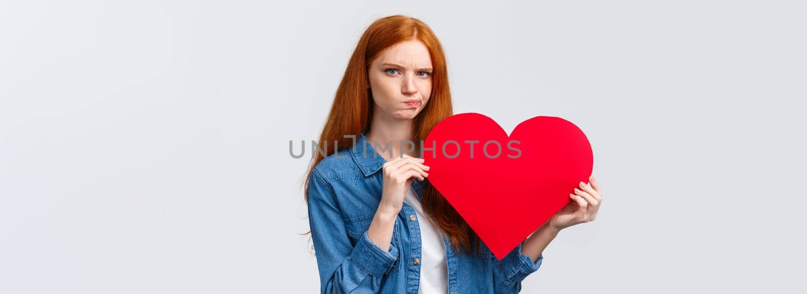 Serious-looking troubled, unsure cute redhead girl thinking what gift buy in addition to valentines day big red heart card, plan romantic date, pouting and frowning camera perplexed by Benzoix