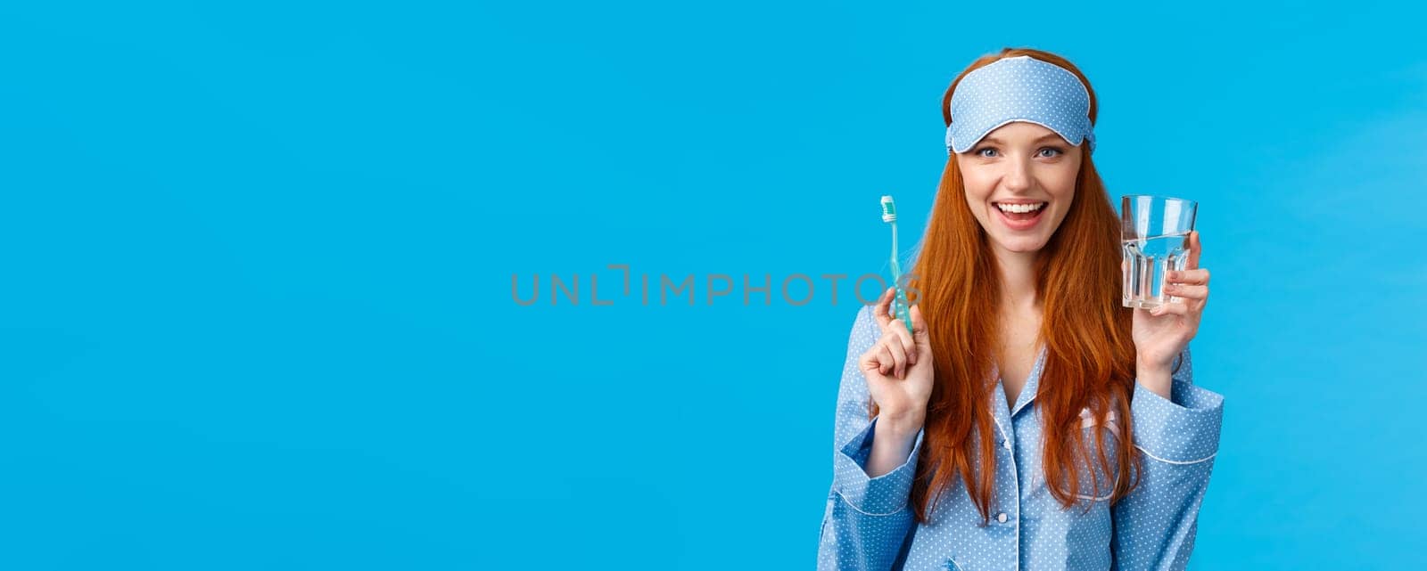 Advertising, hygiene and people concept. Feminine cute redhead girl feeling upbeat and enthusiastic start day right, drinking water, holding glass and toothbrush, wear nightwear and sleep mask by Benzoix