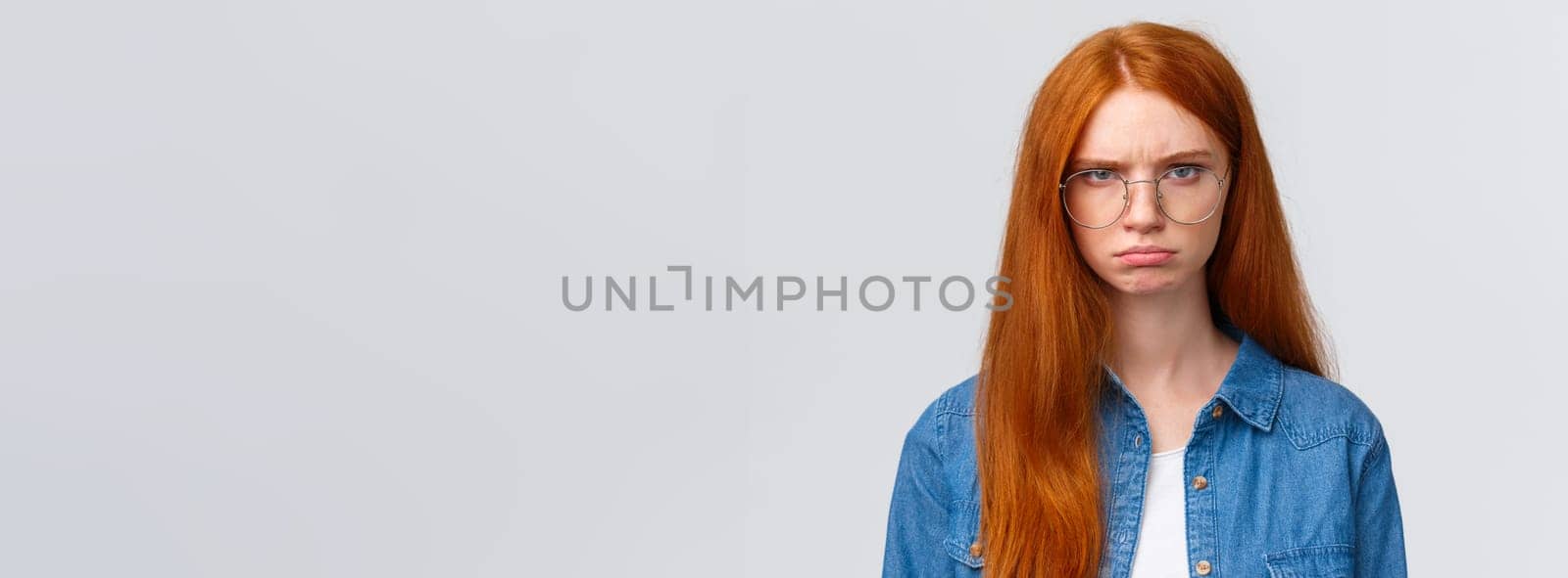 Close-up portrait strict and angry, mad gloomy redhead girl staring offended and disappointed, pouting frowning outraged, condemn something, look skeptical and bothered white background.