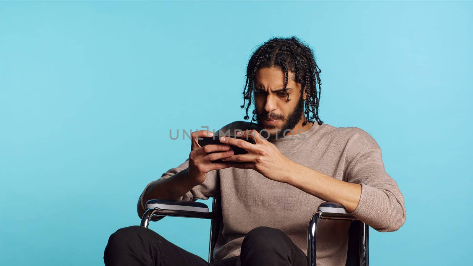 Gamer with disability upset after receiving game over screen on smartphone display. BIPOC man in wheelchair feeling sad after losing videogame, playing on mobile phone, camera A