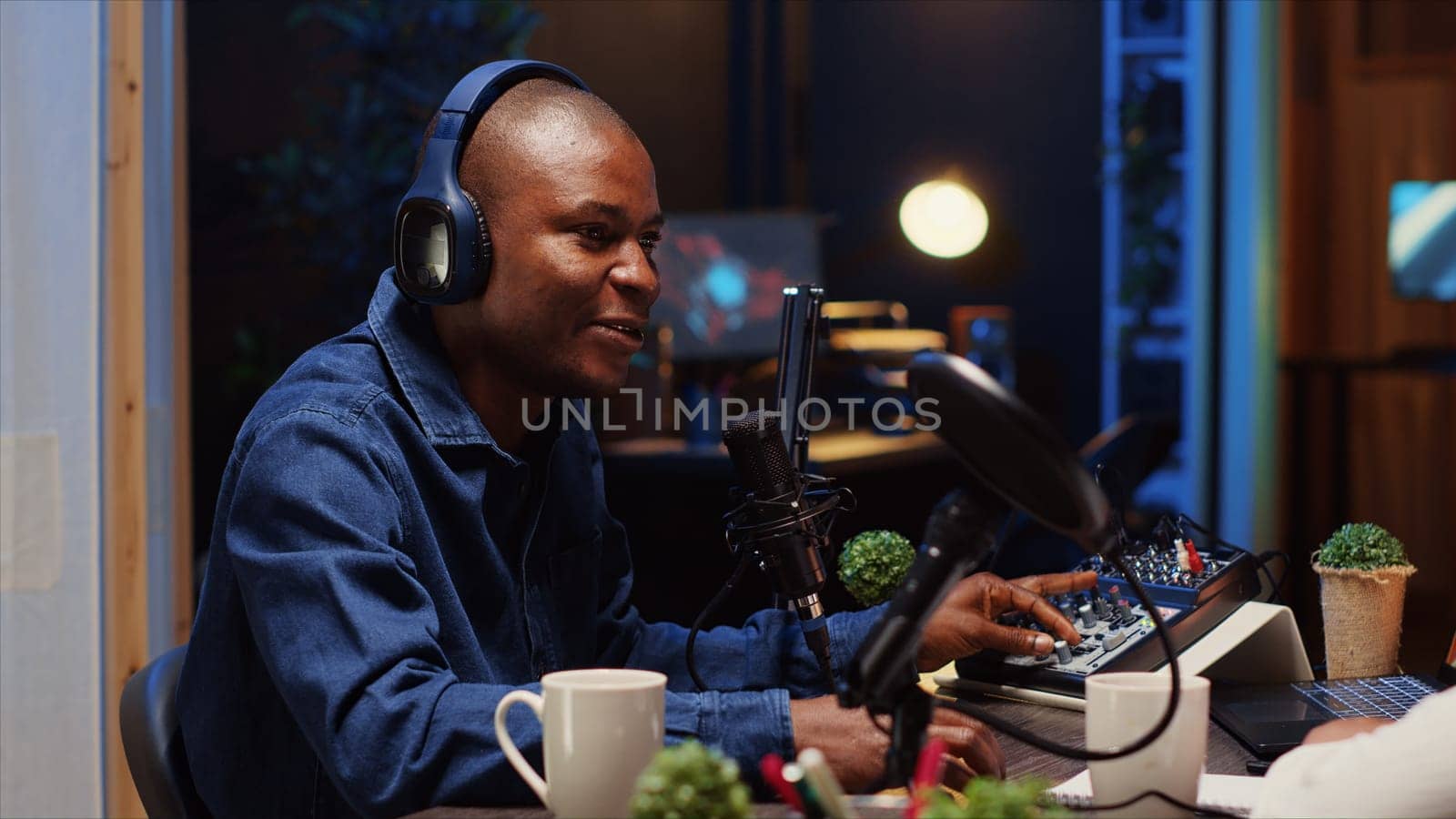 African american man recording podcast, adjusting microphone to ensure optimum sound quality for audience listening at home. Content creator using professional audio producing devices