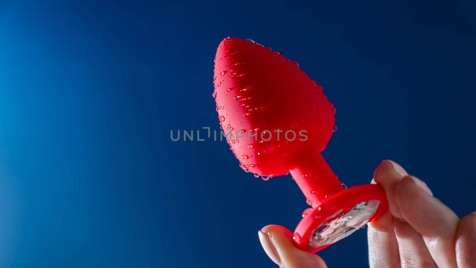 Woman holding red anal plug in water drops on blue background. by mrwed54