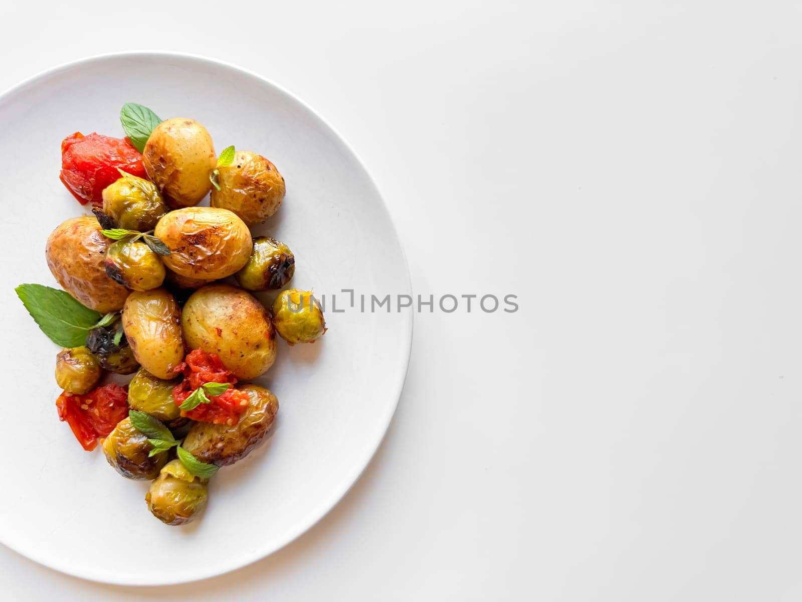 Roasted baby potatoes and Brussels sprouts with cherry tomatoes on white plate, garnished with basil, healthy vegetarian dish concept with space for text. High quality photo