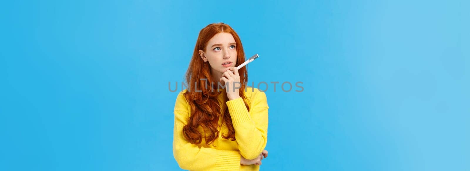 Troubled, hesitant and indecisive redhead, ginger girl with curly hair in yellow sweater, looking unsure upper left corner as pondering, solving exercise in mind, holding pen, searching inspiration by Benzoix