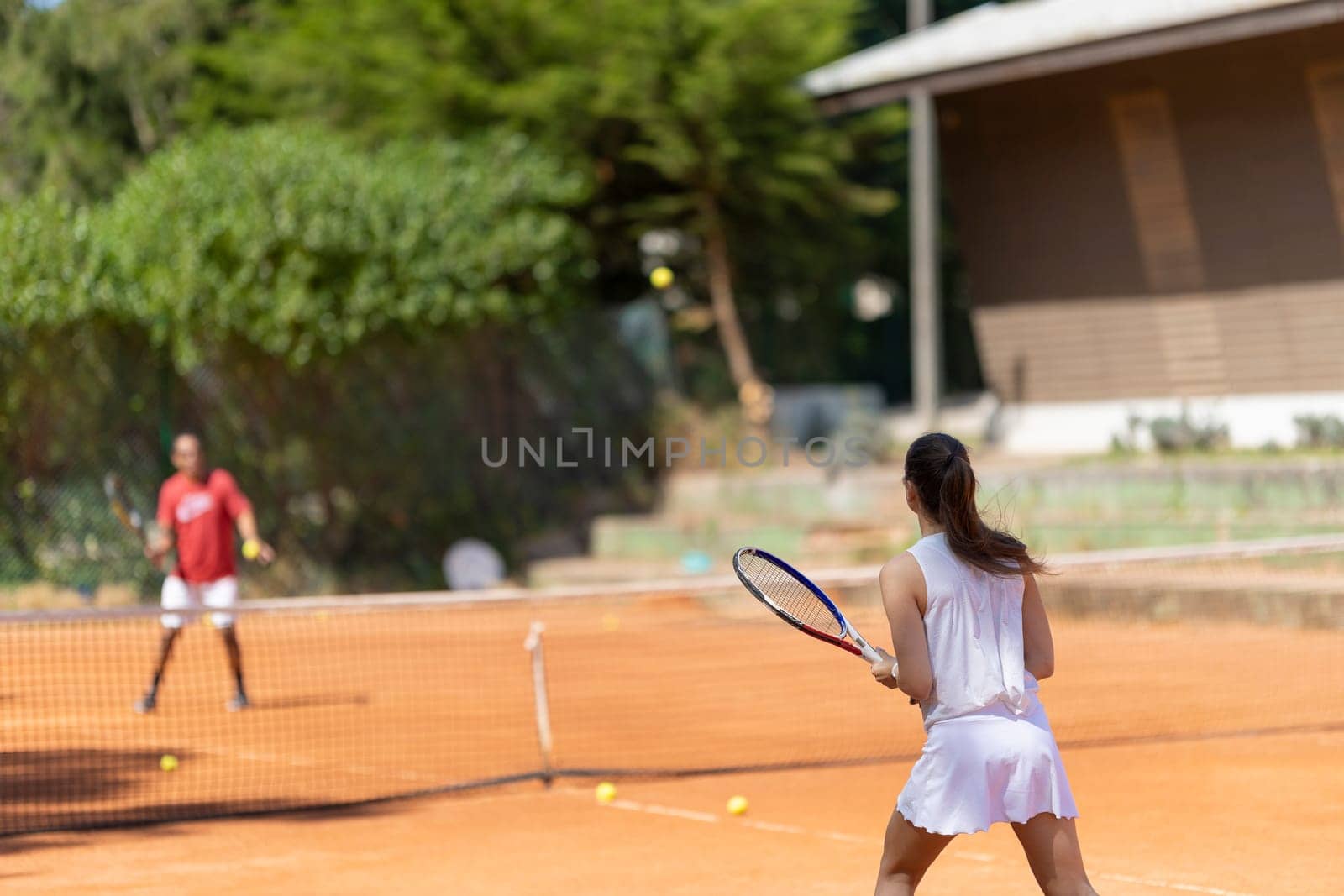 A woman is playing tennis with a man. The woman is wearing a white skirt and is holding a tennis racket