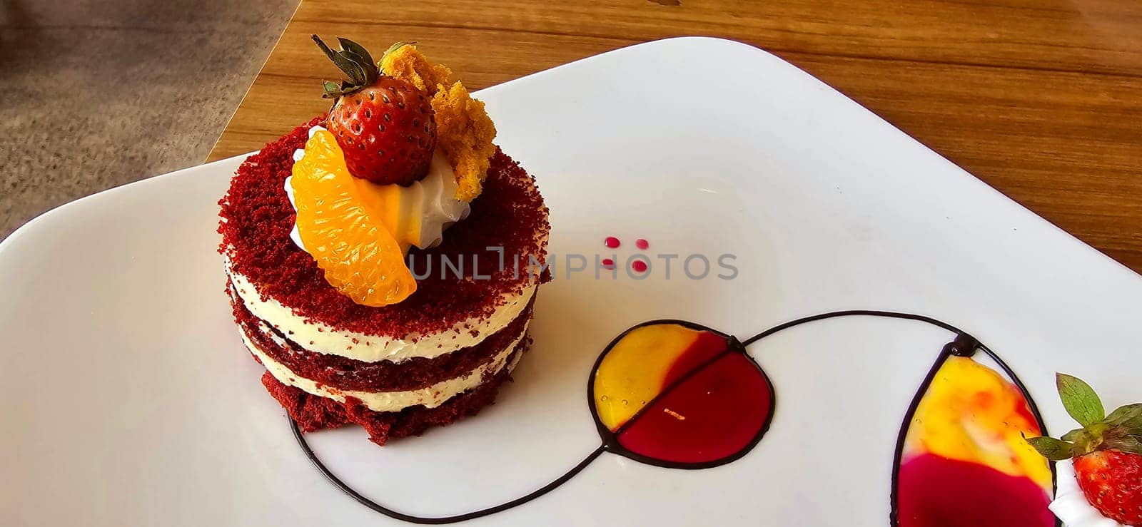 Red velvet cake, classic three layered cake from red butter sponge cakes with cream cheese frosting, with mandarin orange and candied strawberry as topping American cuisine cooking content creation