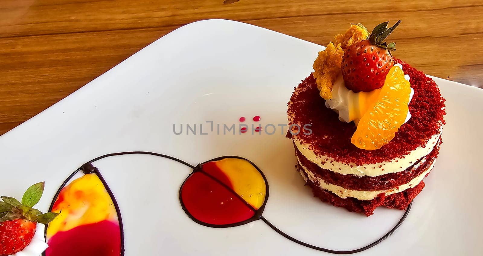 Red velvet cake, classic three layered cake from red butter sponge cakes with cream cheese frosting, with mandarin orange and candied strawberry as topping American cuisine cooking content creation