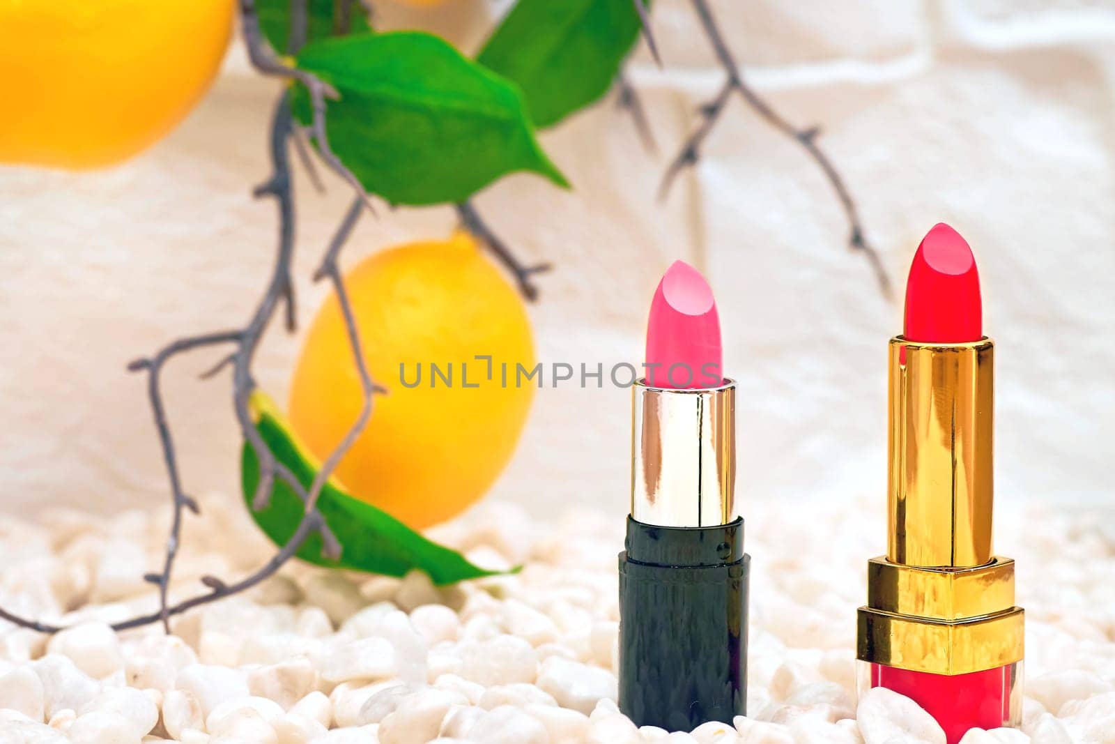 Two red pink lipsticks on yellow pebbles stones with lemon branch by jovani68