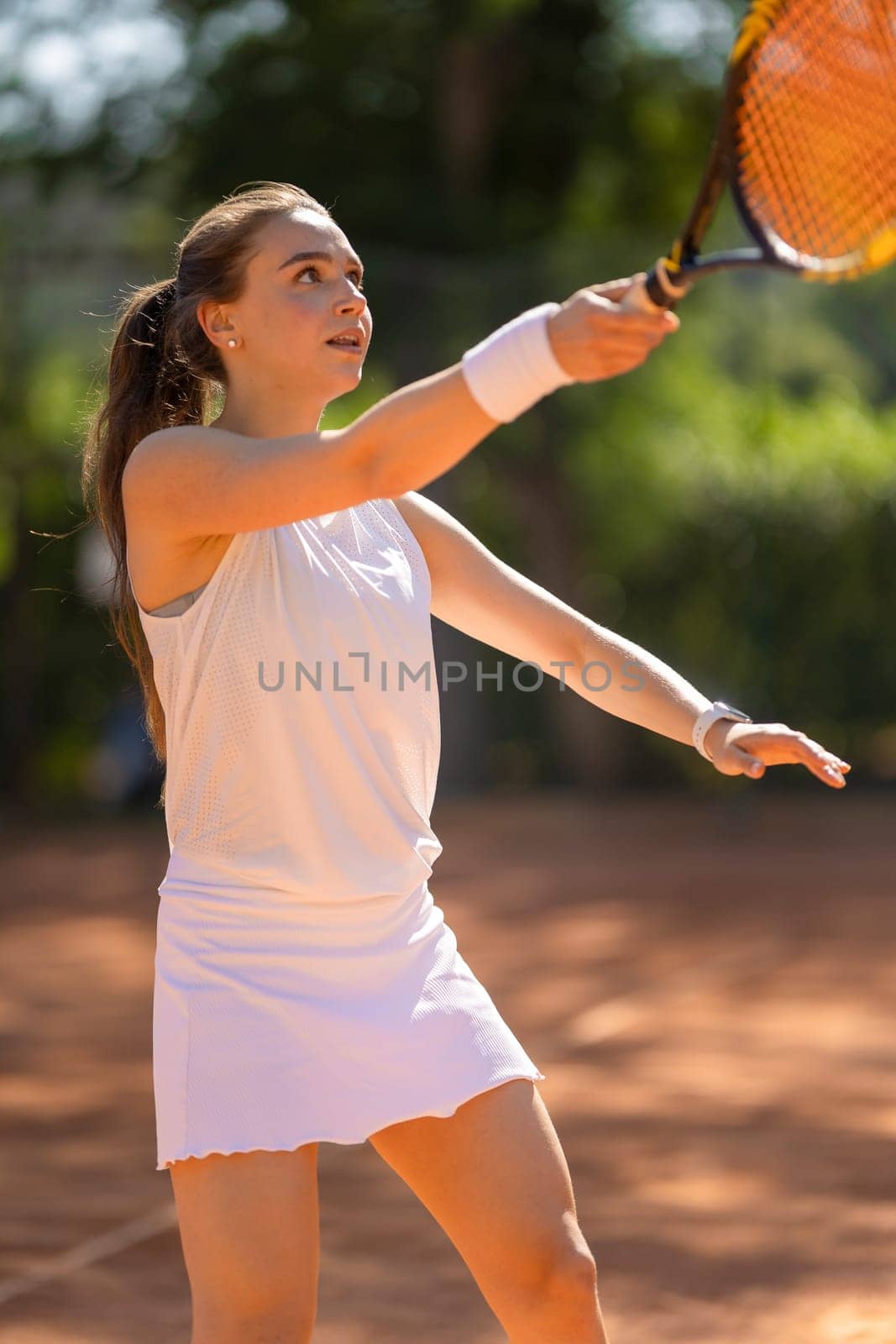 A woman is playing tennis on a court. She is wearing a white shirt and a white skirt