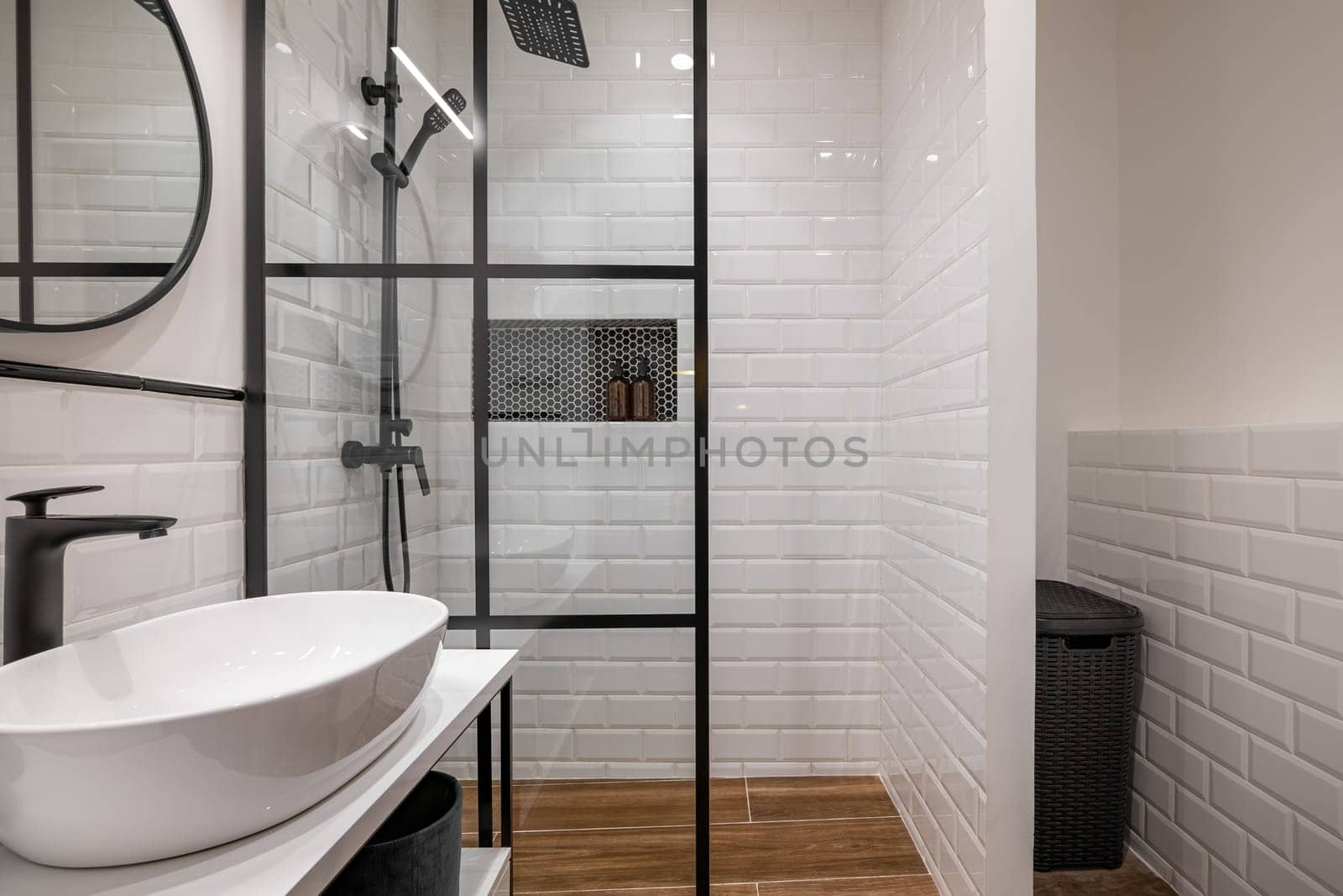 Stylish modern bathroom featuring glass shower enclosure, white subway tile walls, and wooden flooring. Elegant black fixtures and a minimalist design aesthetic.