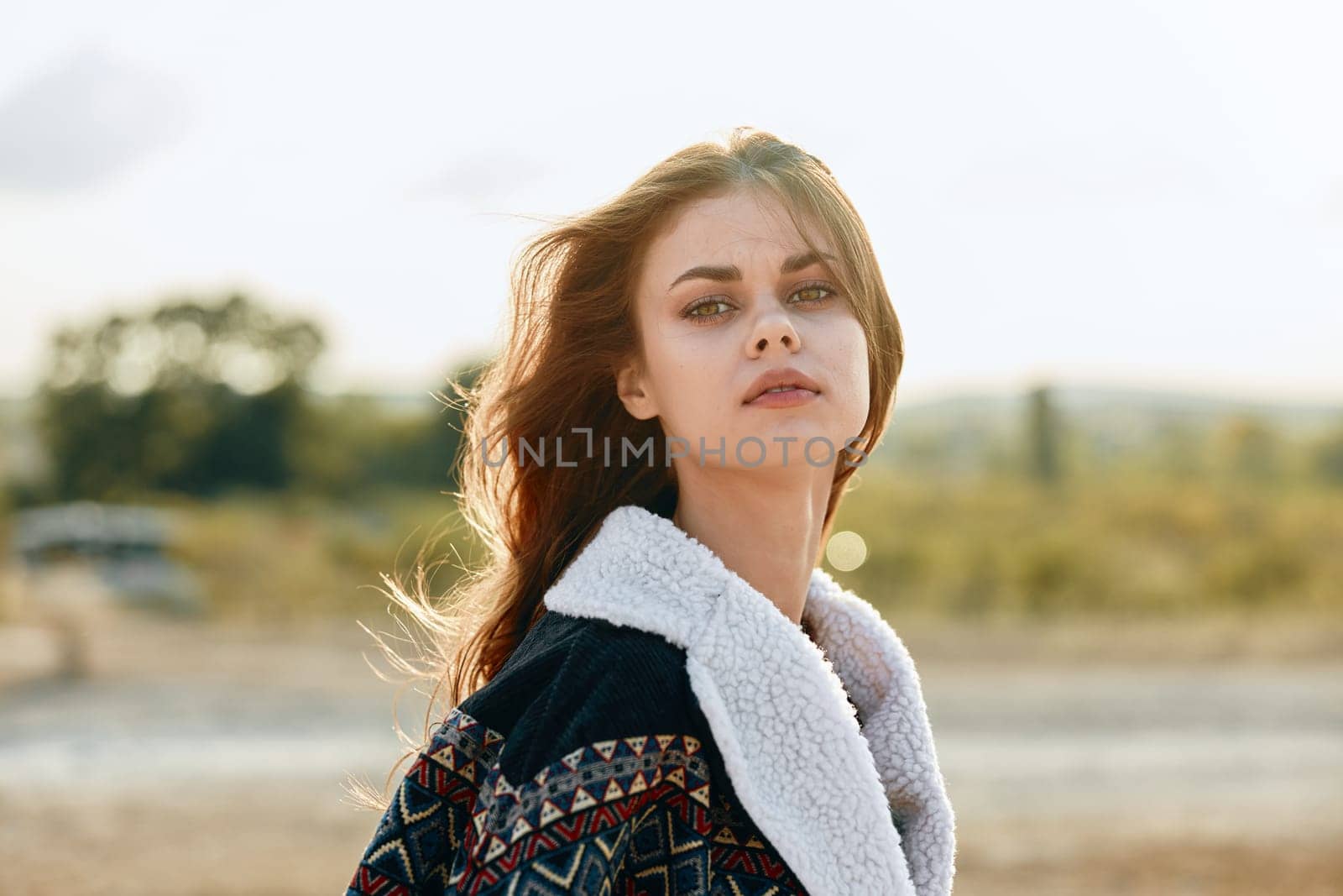 Serene woman with flowing hair standing in a sunlit field at dusk